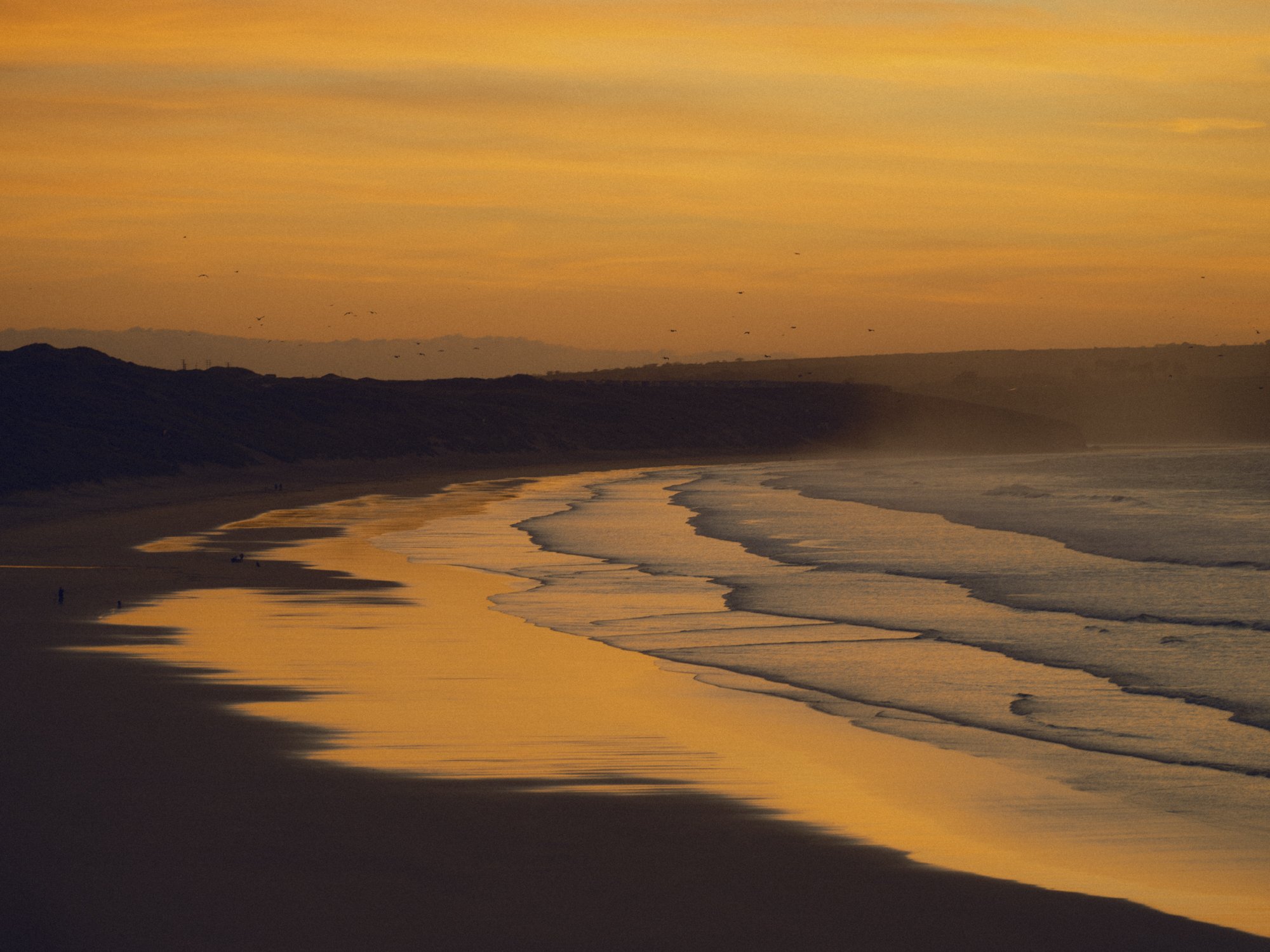 Sunset over a beach with waves hitting the shore and a colorful sky.