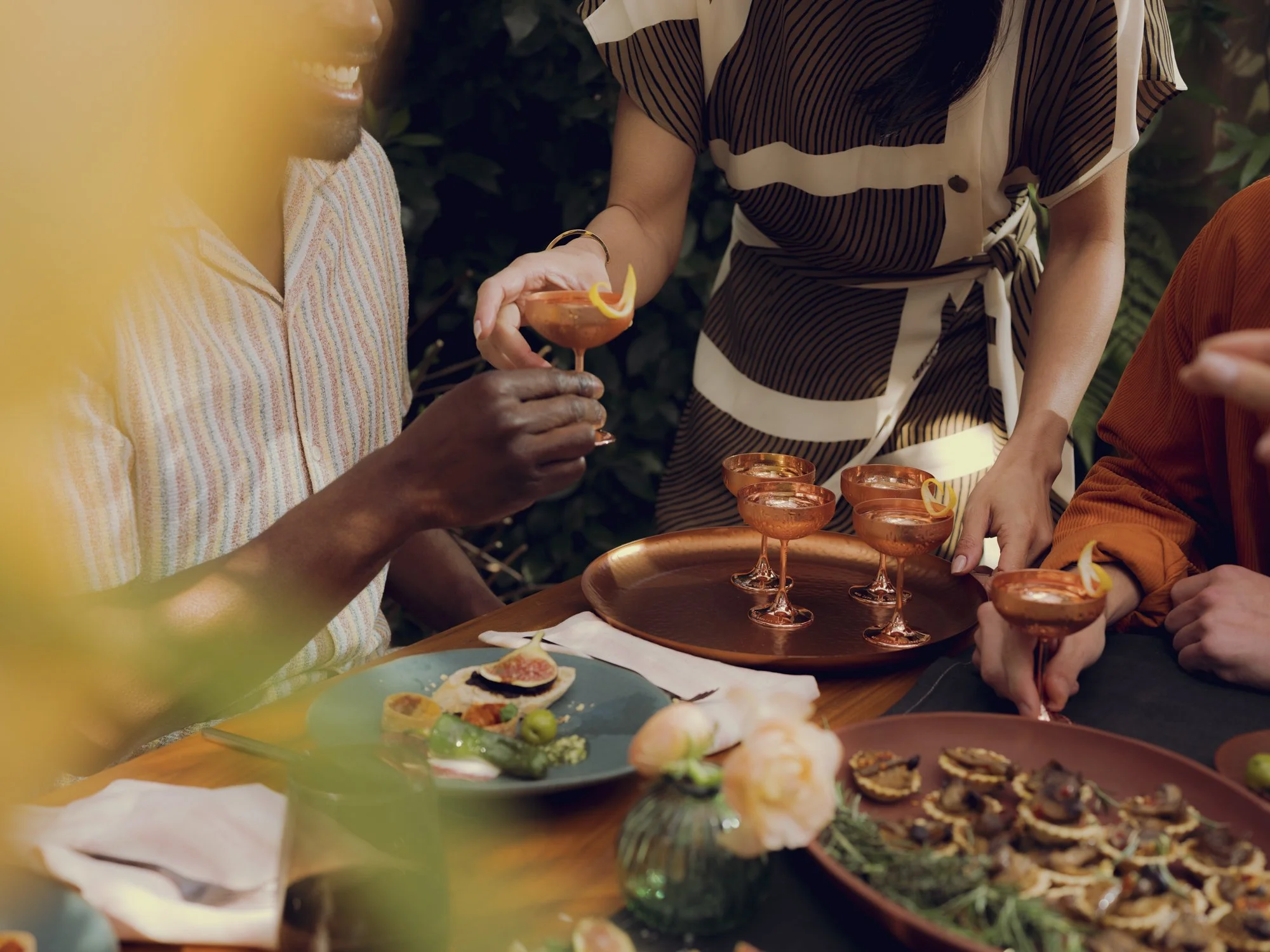 People enjoying drinks and food at a gathering, with one person passing around cocktail glasses with lemon garnishes.