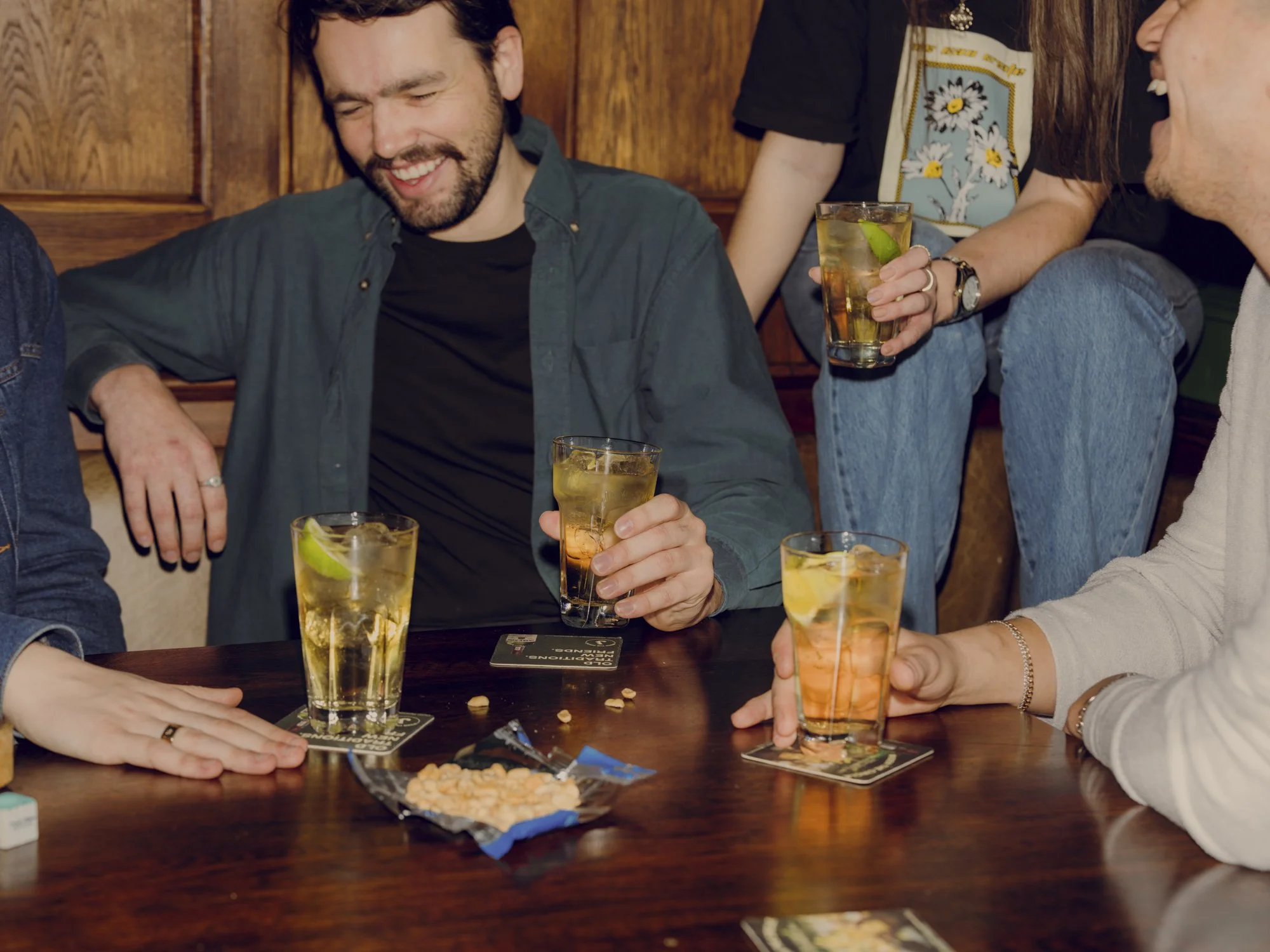 People gathered around a table with drinks, snacks, and socializing in a cozy pub or bar setting.