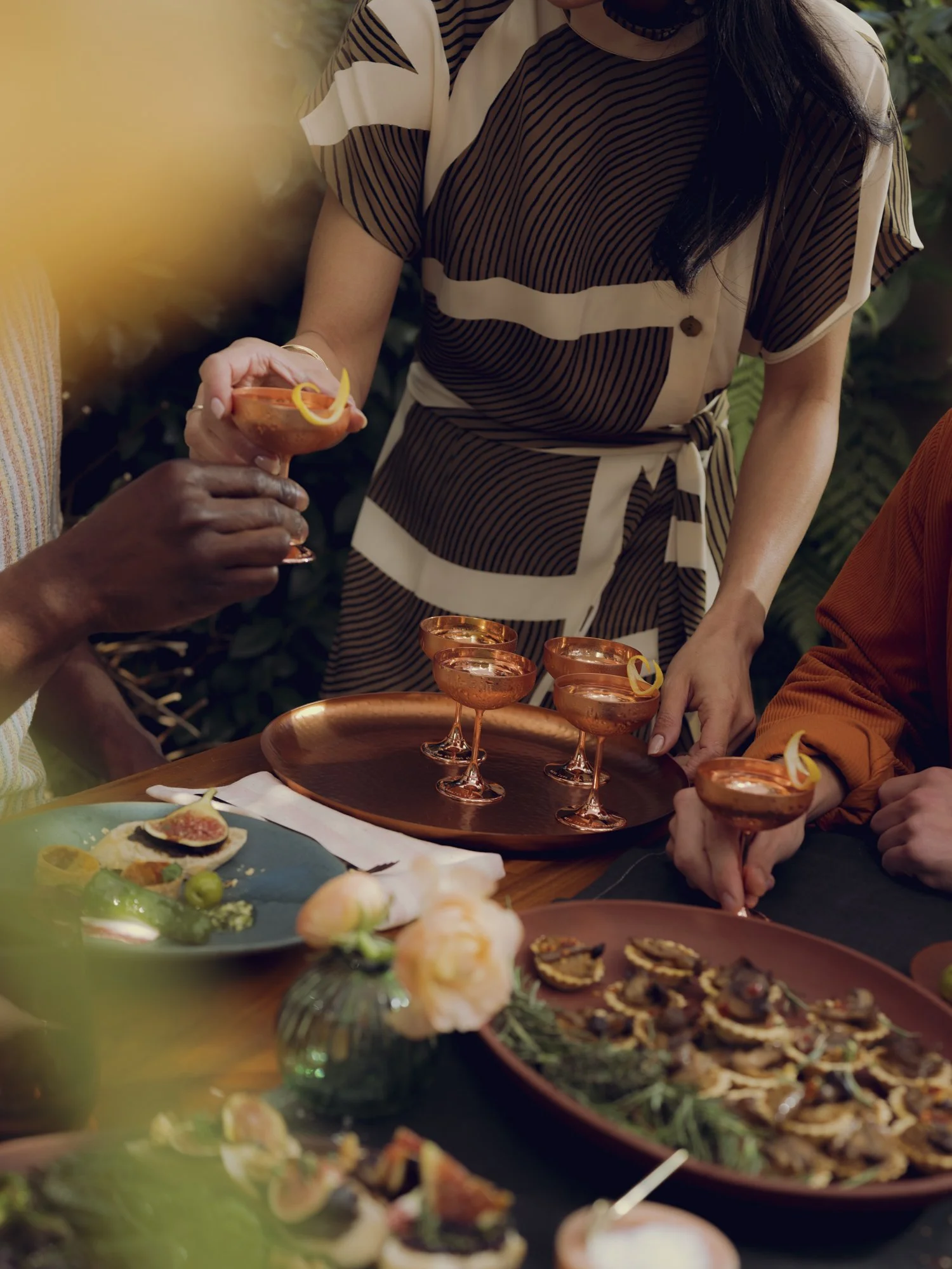 People at a gathering enjoying cocktails and appetizers at a table filled with food and drinks.