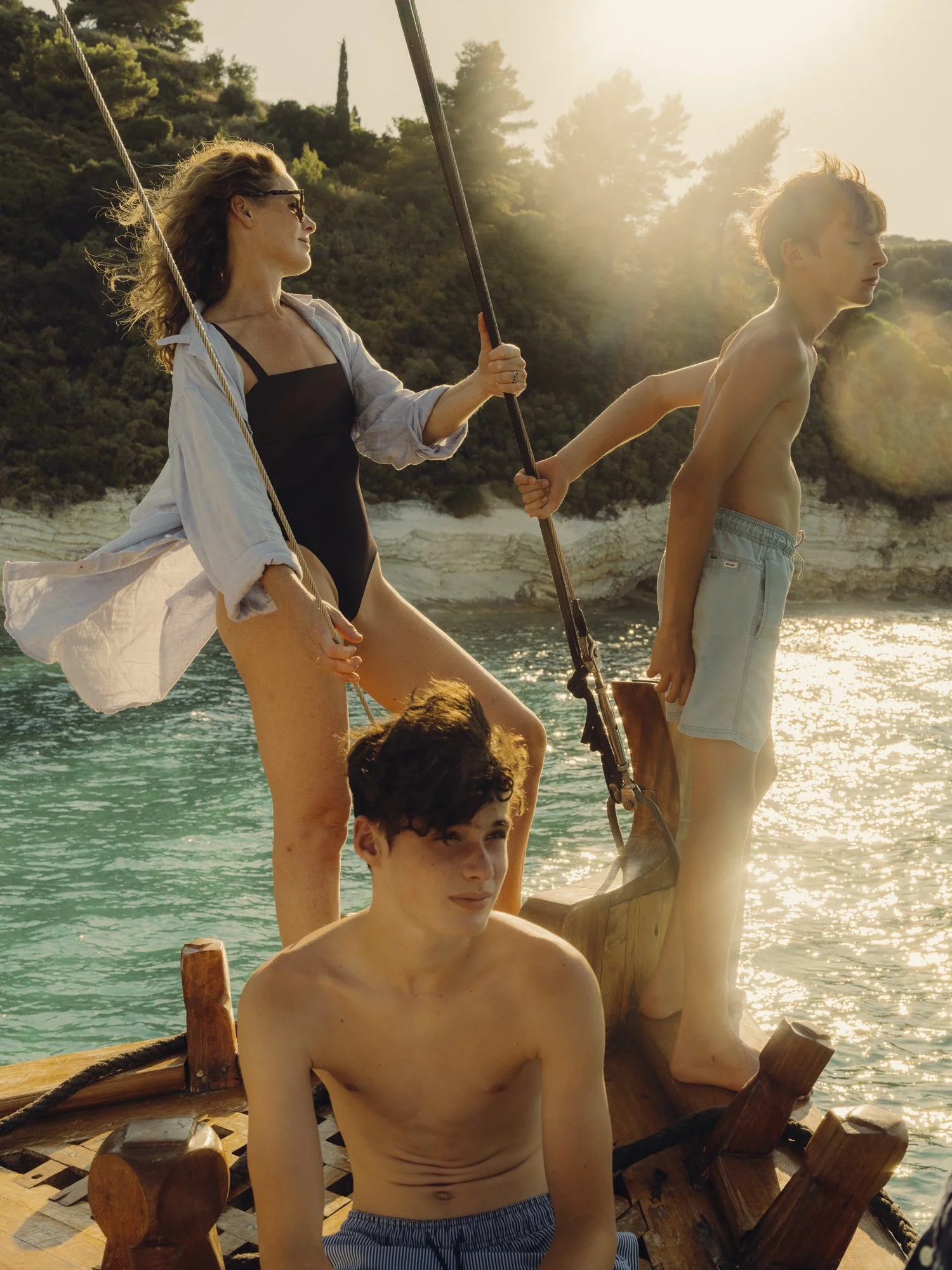 Two women and two young men on a boat, with water and cliffs in the background, during sunset, dressed casually for summer.
