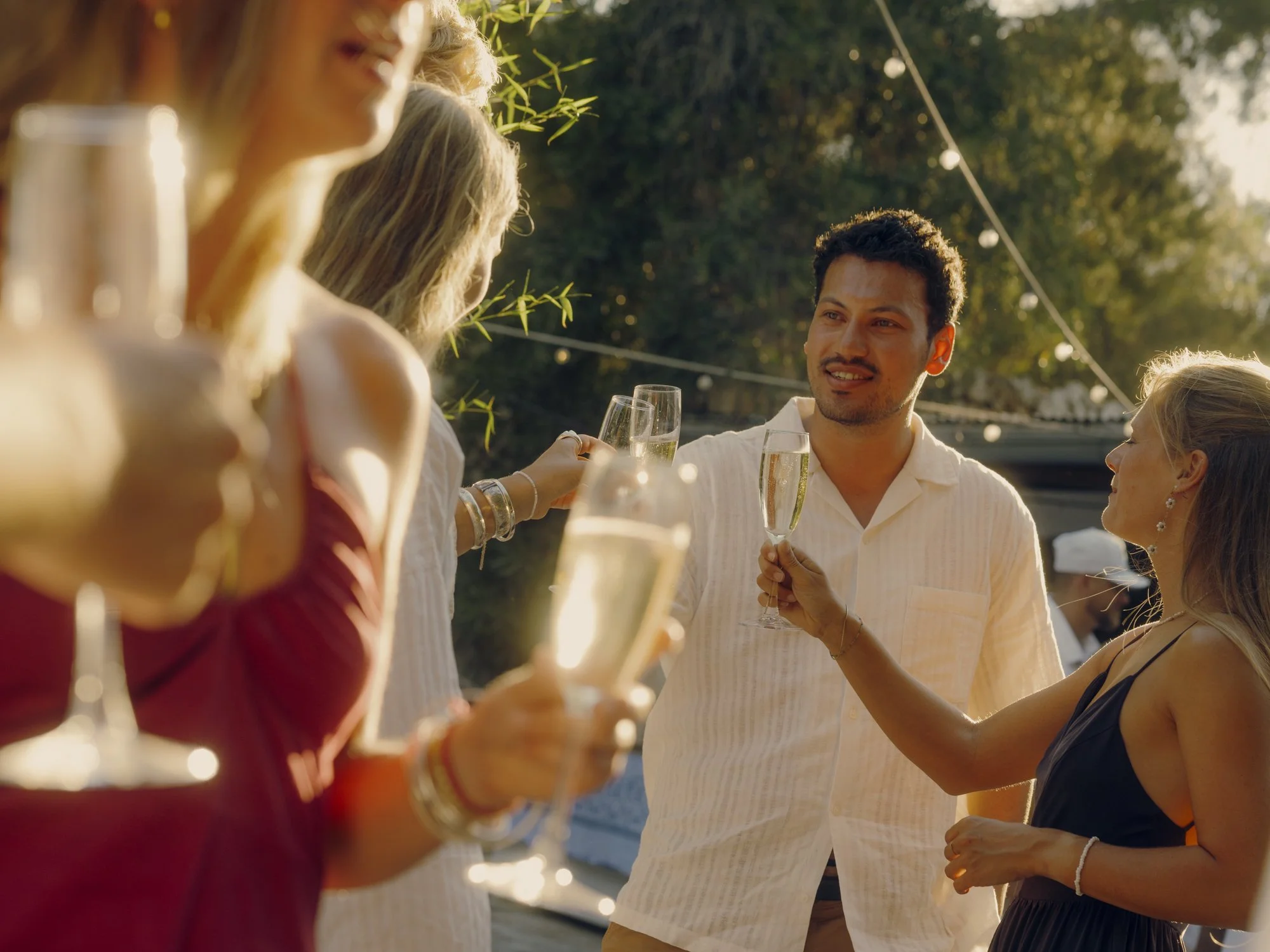 People at an outdoor gathering raising glasses of champagne during sunset