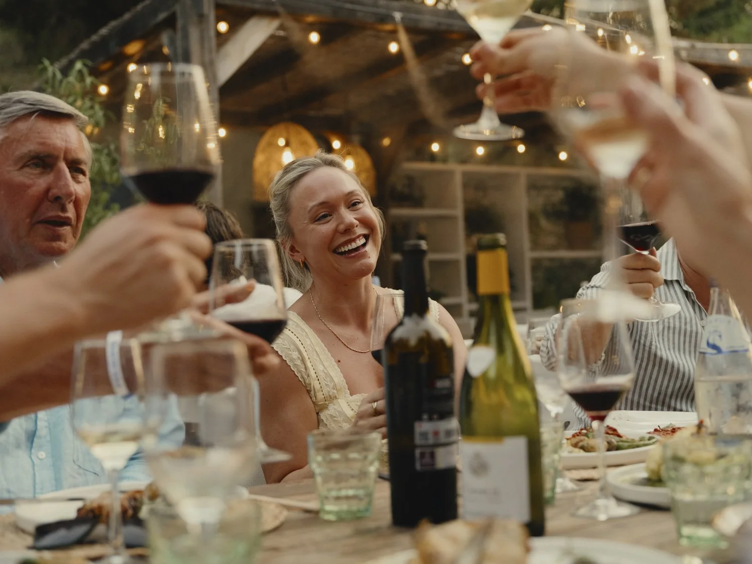 People enjoying a dinner party outdoors, raising glasses of wine in a toast at sunset.