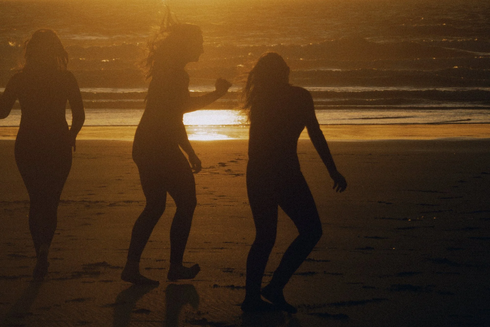 Silhouettes of three women walking on the beach during sunset.