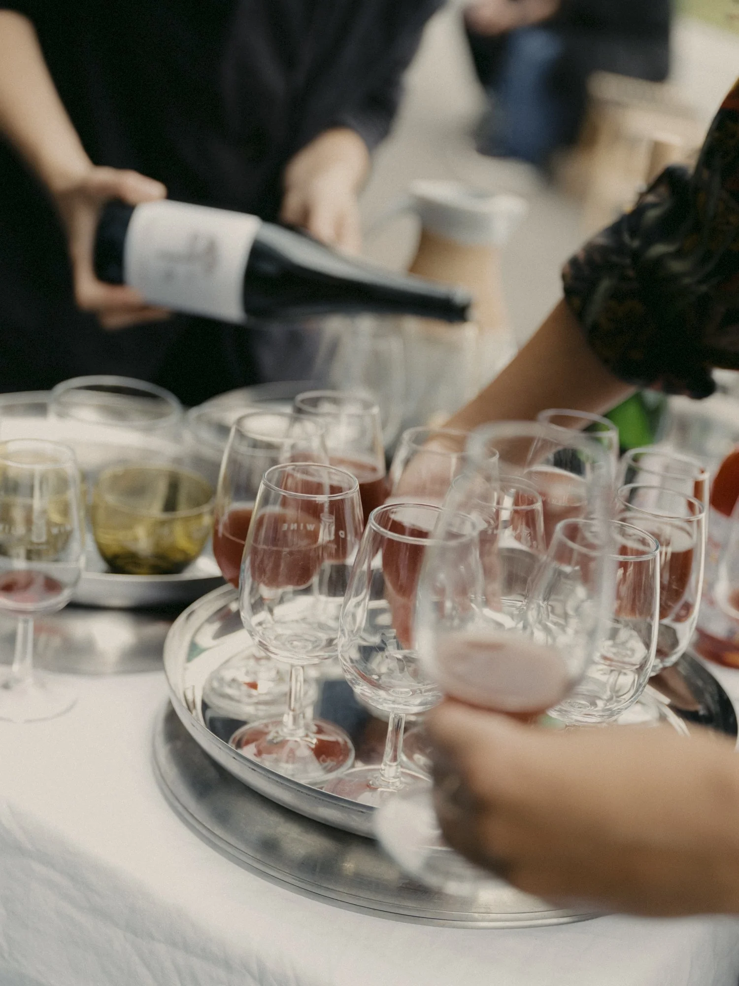 People pouring wine and placing glasses on a tray at a social gathering.