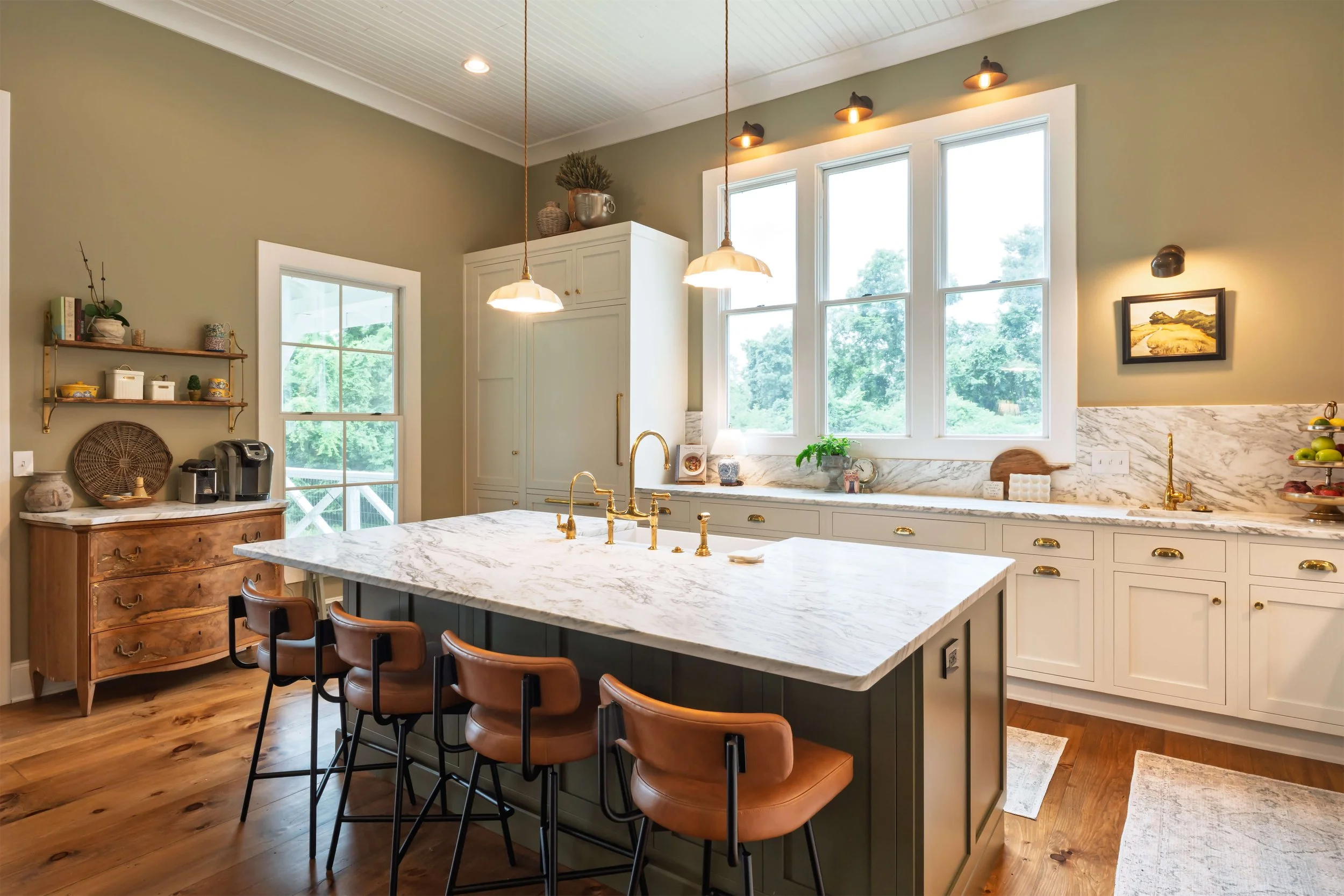 A kitchen featuring a built-in refrigerator, panel ready refrigerator, an island with marble countertops, a hood above the stove, and inset cabinetry, illuminated by pendant lights. Island chairs are next to the island.