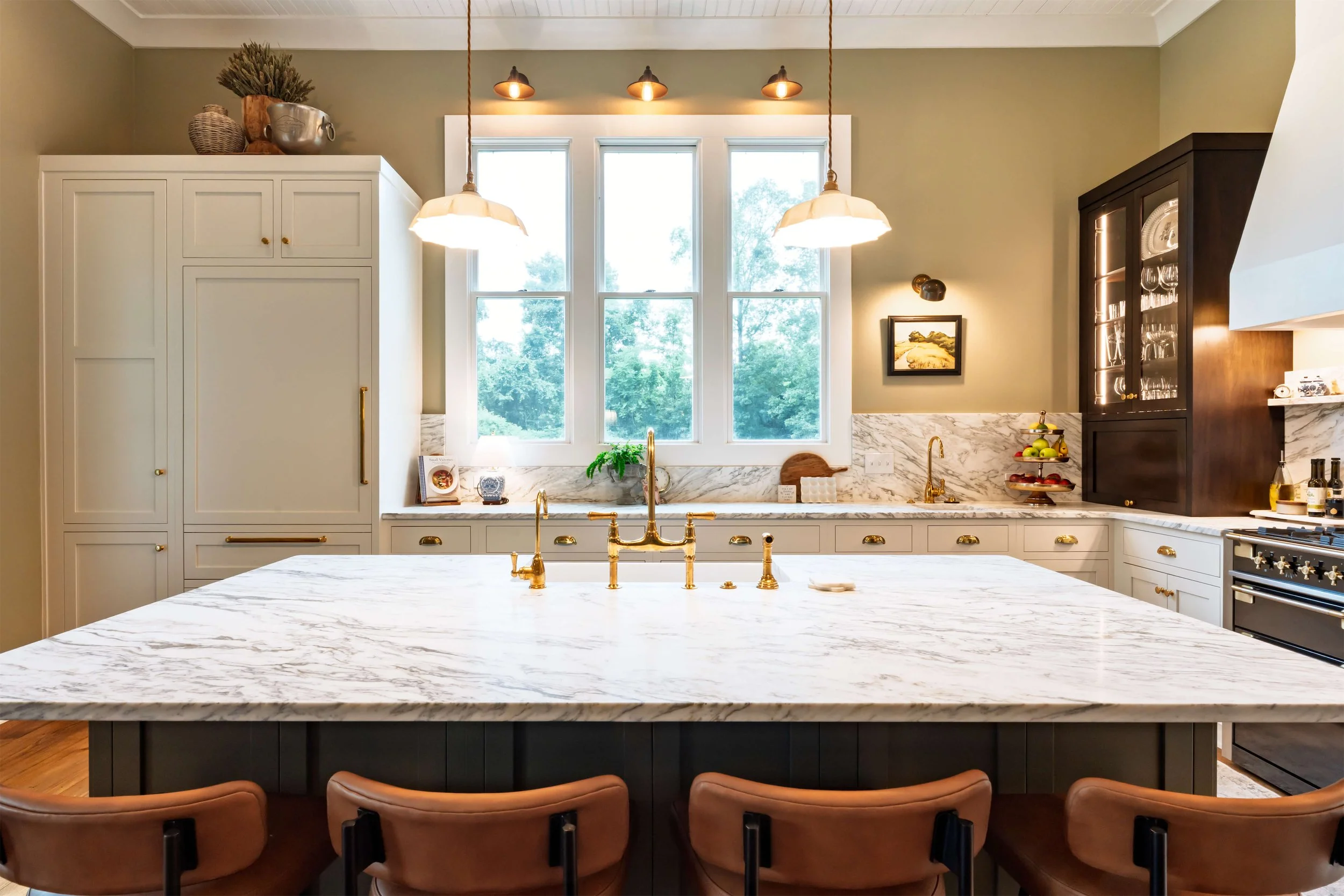 A modern kitchen featuring a built-in refrigerator, panel ready refrigerator, an island with marble countertops, a hood above the stove, and inset cabinetry, illuminated by pendant lights.