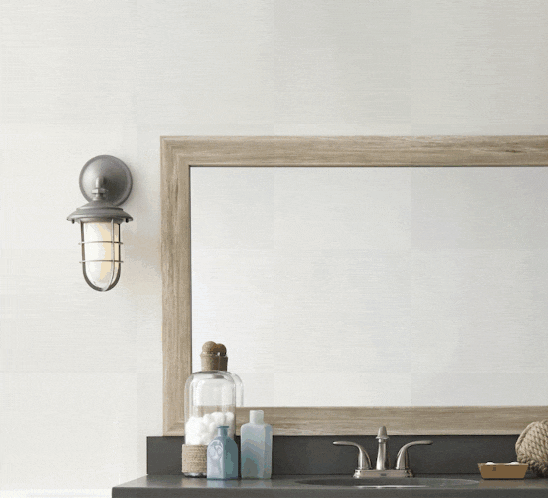 Bathroom vanity with mirror, single wall sconce, faucet, storage jars, and bottles.
