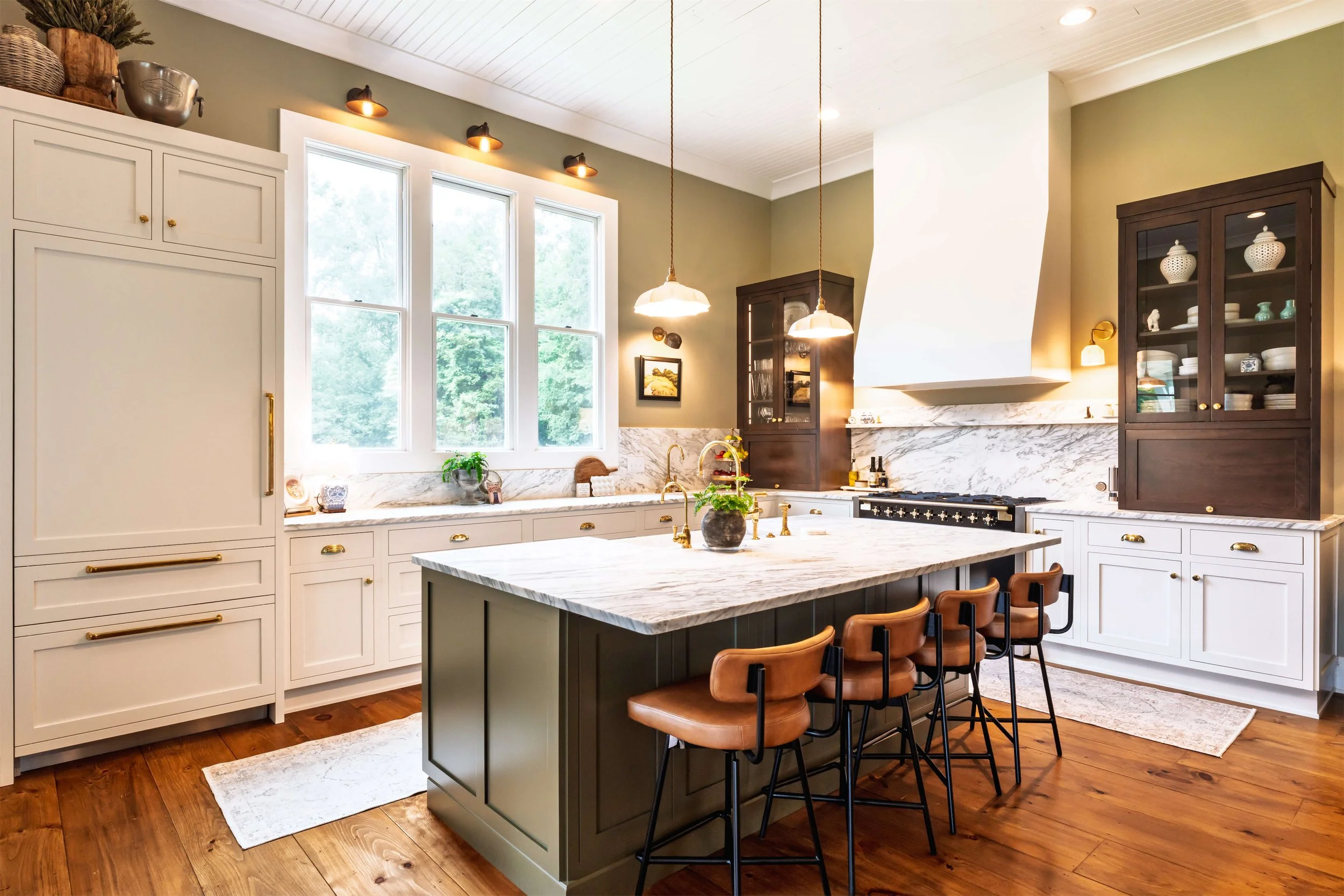 A modern kitchen featuring a built-in refrigerator, panel ready refrigerator, an island with marble countertops, a hood above the stove, and inset cabinetry, illuminated by pendant lights.