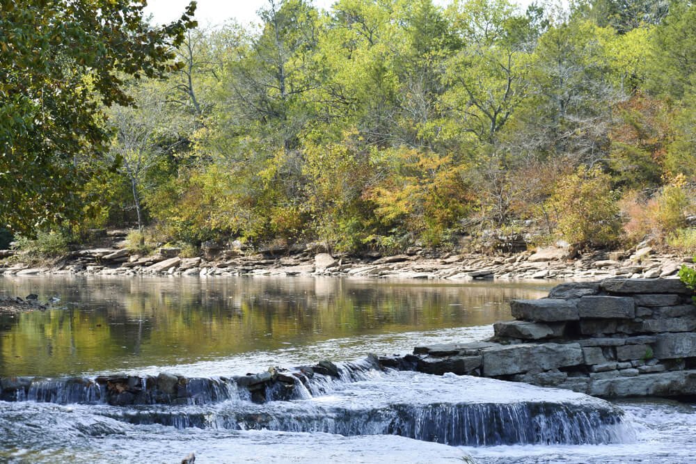 Scenic view of a small waterfall in a river surrounded by autumn trees and rocks.