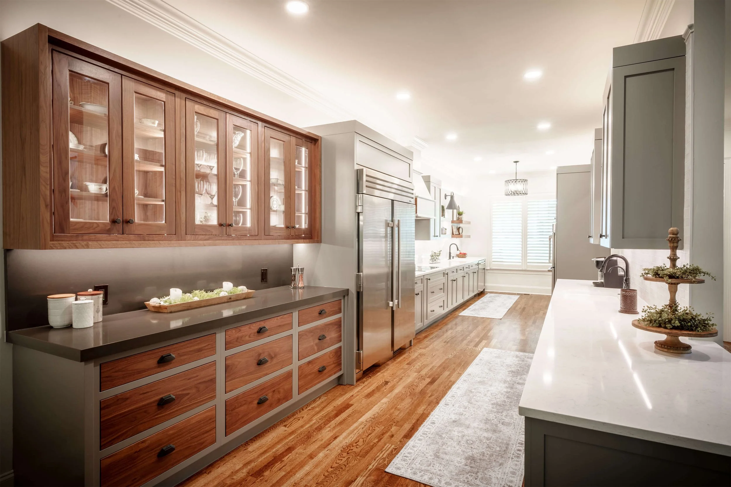 Bright kitchen with white and wooden cabinetry, stainless steel appliances, hardwood floors, and large windows with white blinds.
