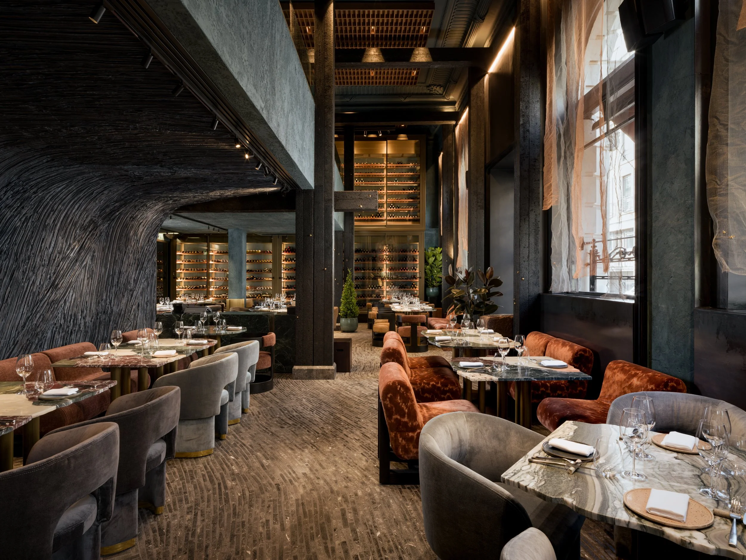 Luxury restaurant interior with double-height wine display, textured timber architecture and marble tables, photographed by a London interior photographer specialising in hospitality and architectural photography.