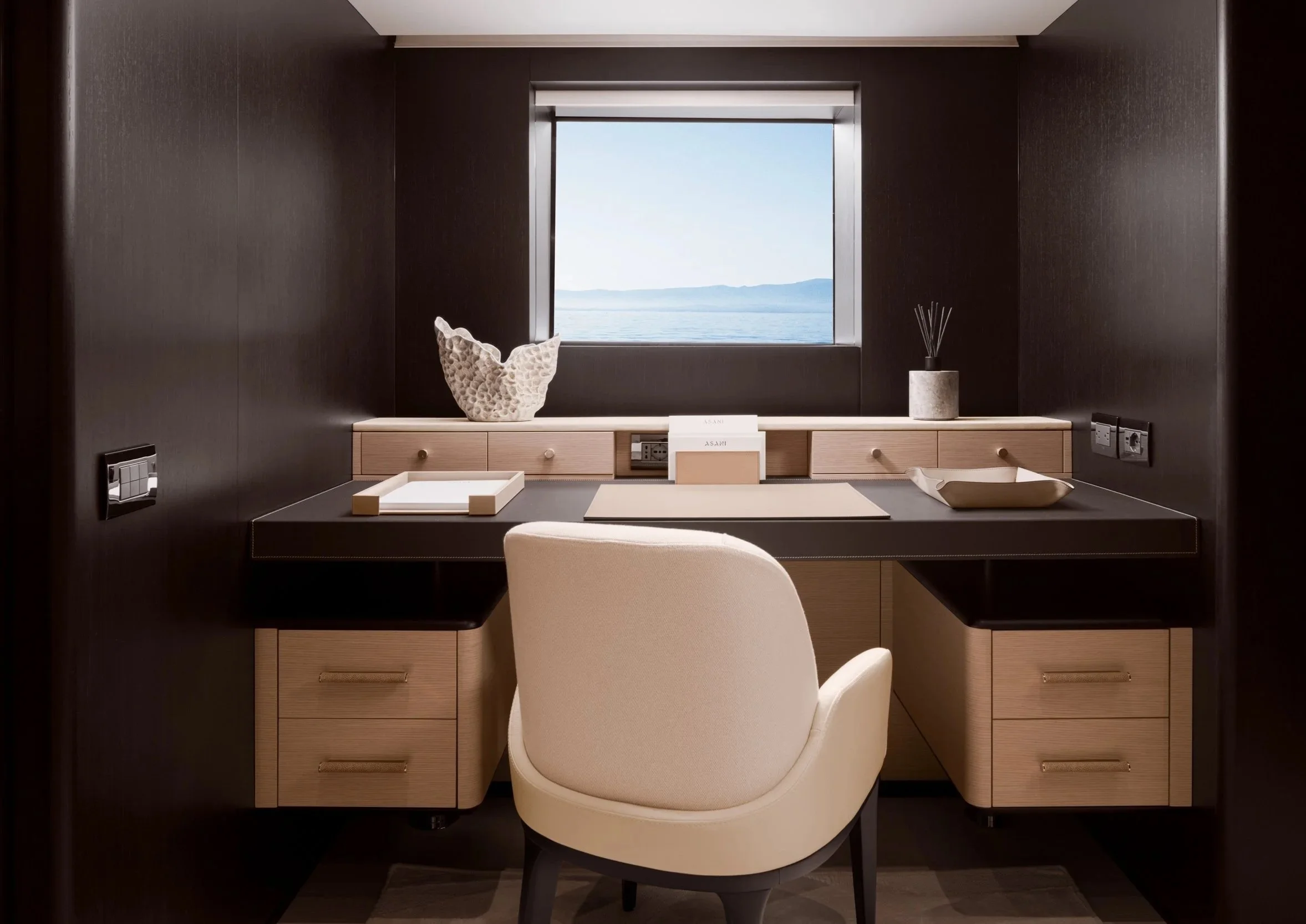 Luxury workspace with a sleek built-in desk, dark wood paneling, and a panoramic ocean view, showcasing contemporary hospitality and interior design photography.