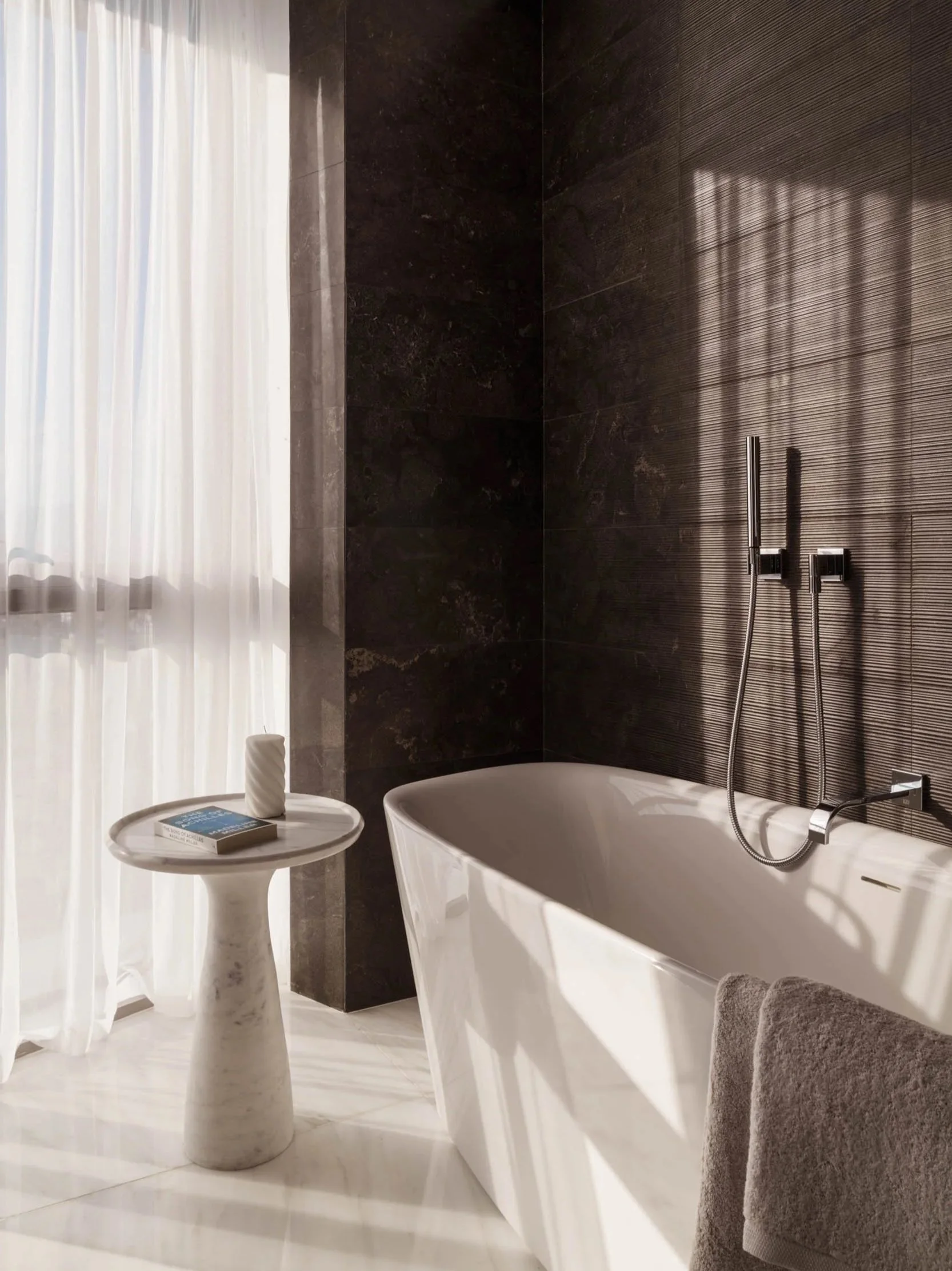 Modern luxury bathroom with freestanding bathtub, dark textured walls, and natural light, captured by an interior design photographer.