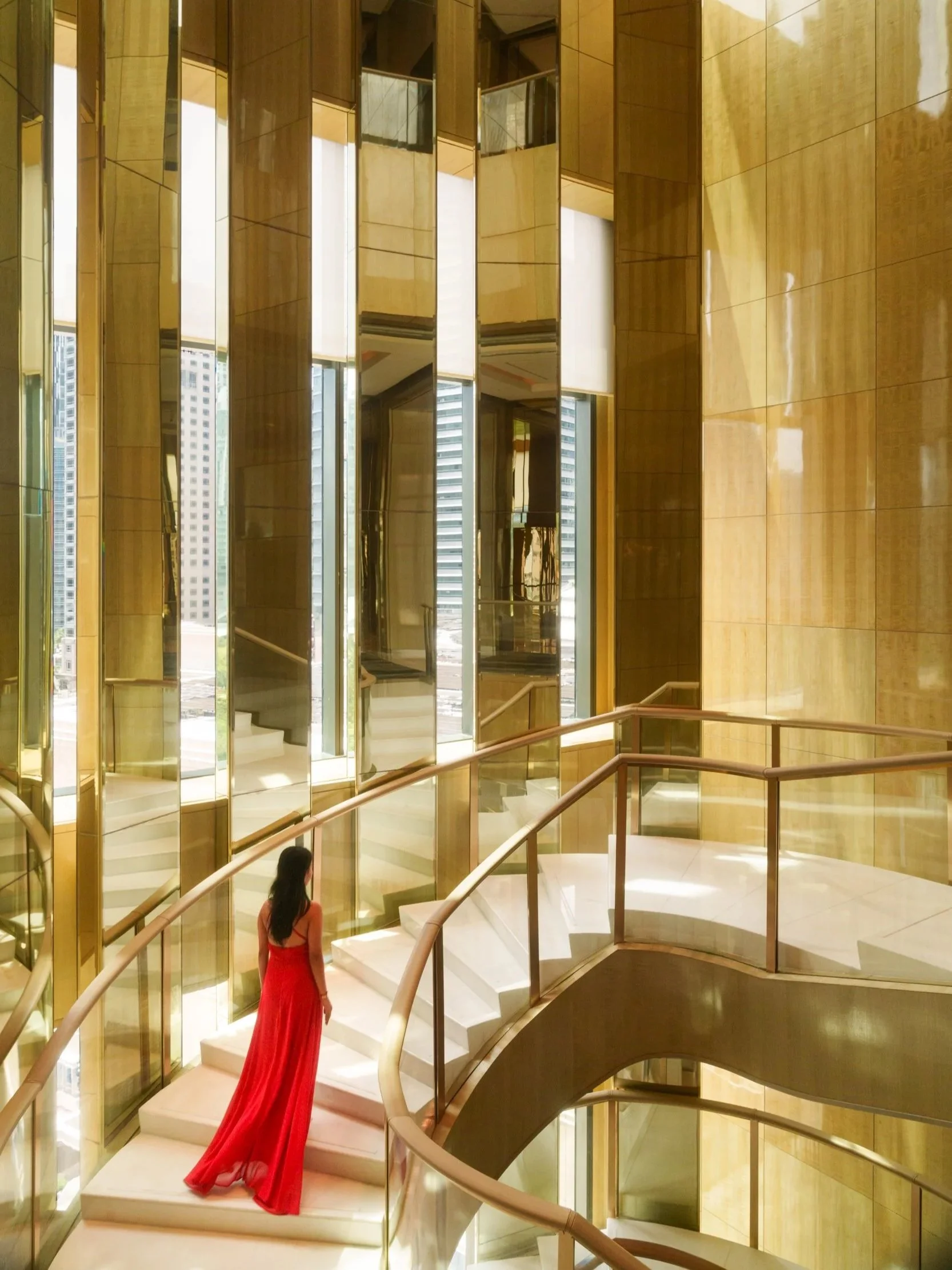 Elegant hotel interior featuring a grand curved staircase with gold-accented mirrored walls, illuminated by natural light, showcasing luxury hospitality and architectural design photography.