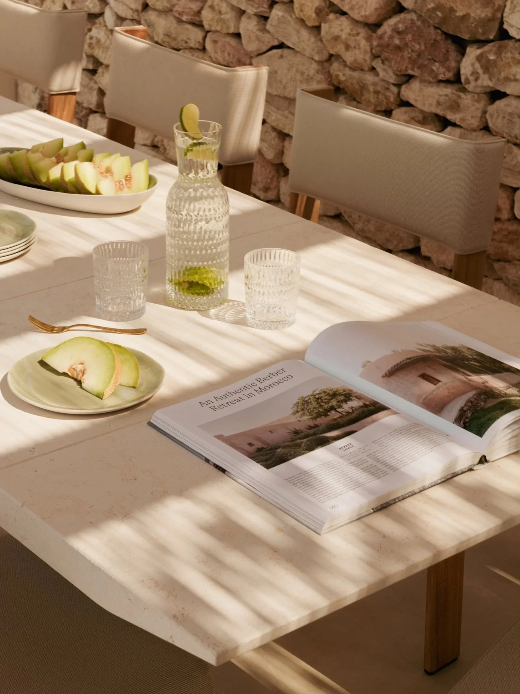 Interior photography of an elegant dining setup in Surrey, featuring a textured stone wall, natural light, and a beautifully styled table with fresh melon and glassware.
