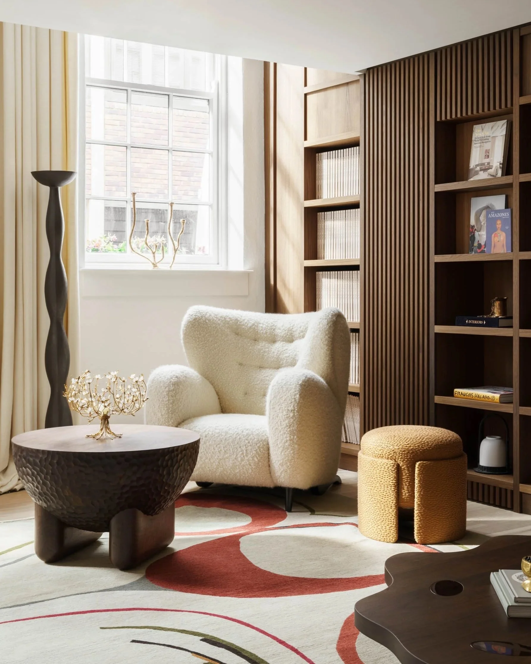 Contemporary reading nook with a boucle armchair, sculptural wooden coffee table, and custom shelving. This inviting space, bathed in natural light, was photographed by a London interior design photographer.