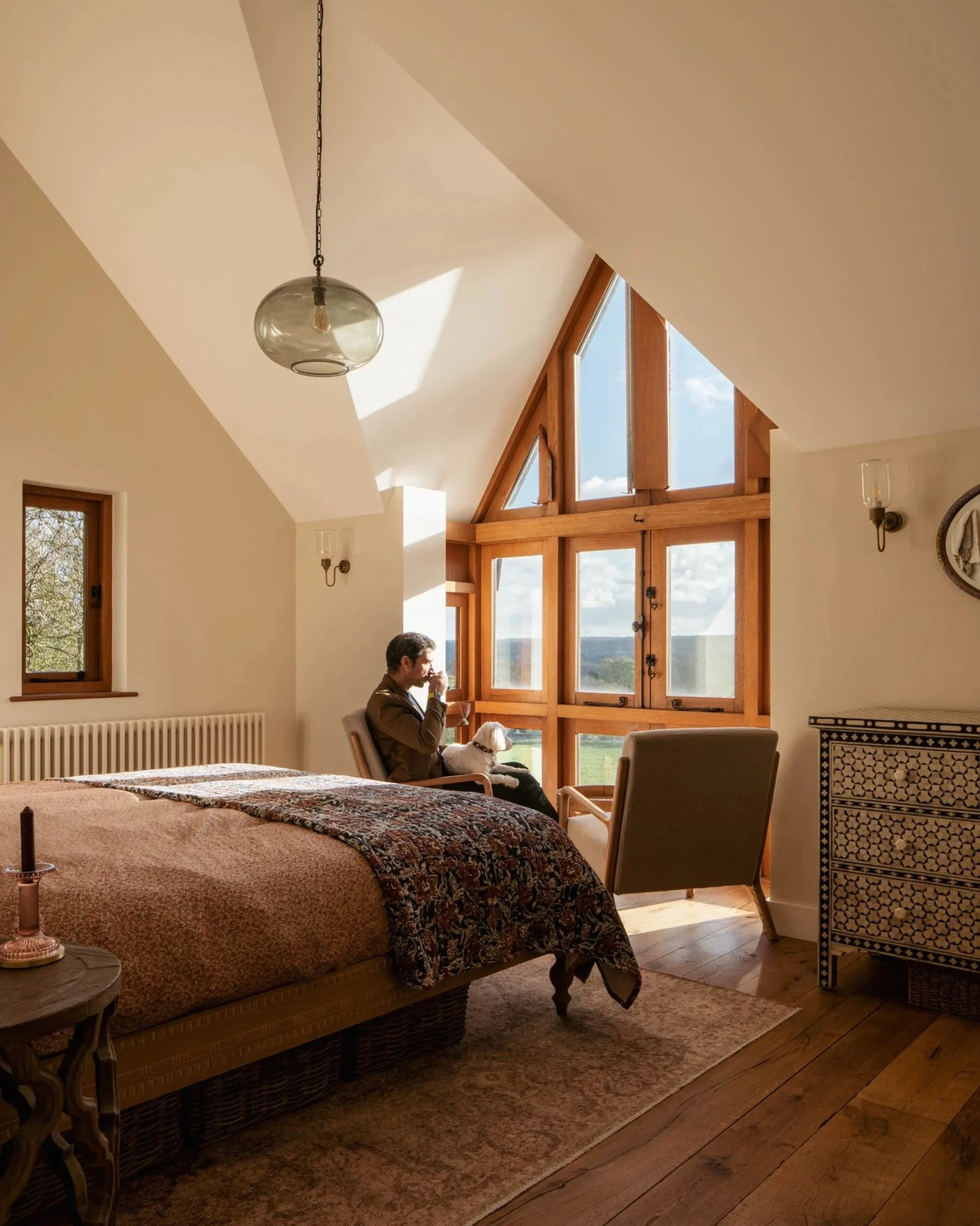 Warm and inviting bedroom with vaulted ceilings, large timber-framed windows, and natural light. The rustic design blends modern comfort with traditional charm.
