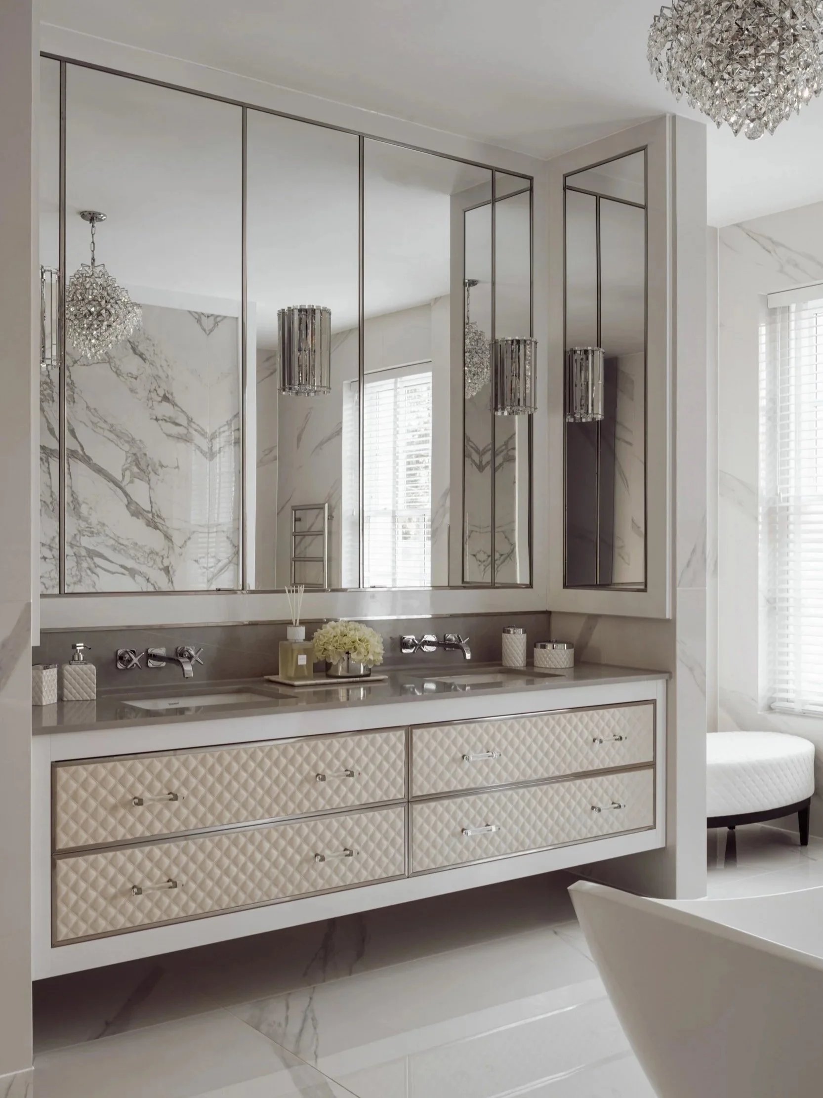 Elegant marble-clad bathroom in London featuring a custom quilted vanity, mirrored cabinets, and a crystal chandelier reflecting in the glossy surfaces.
