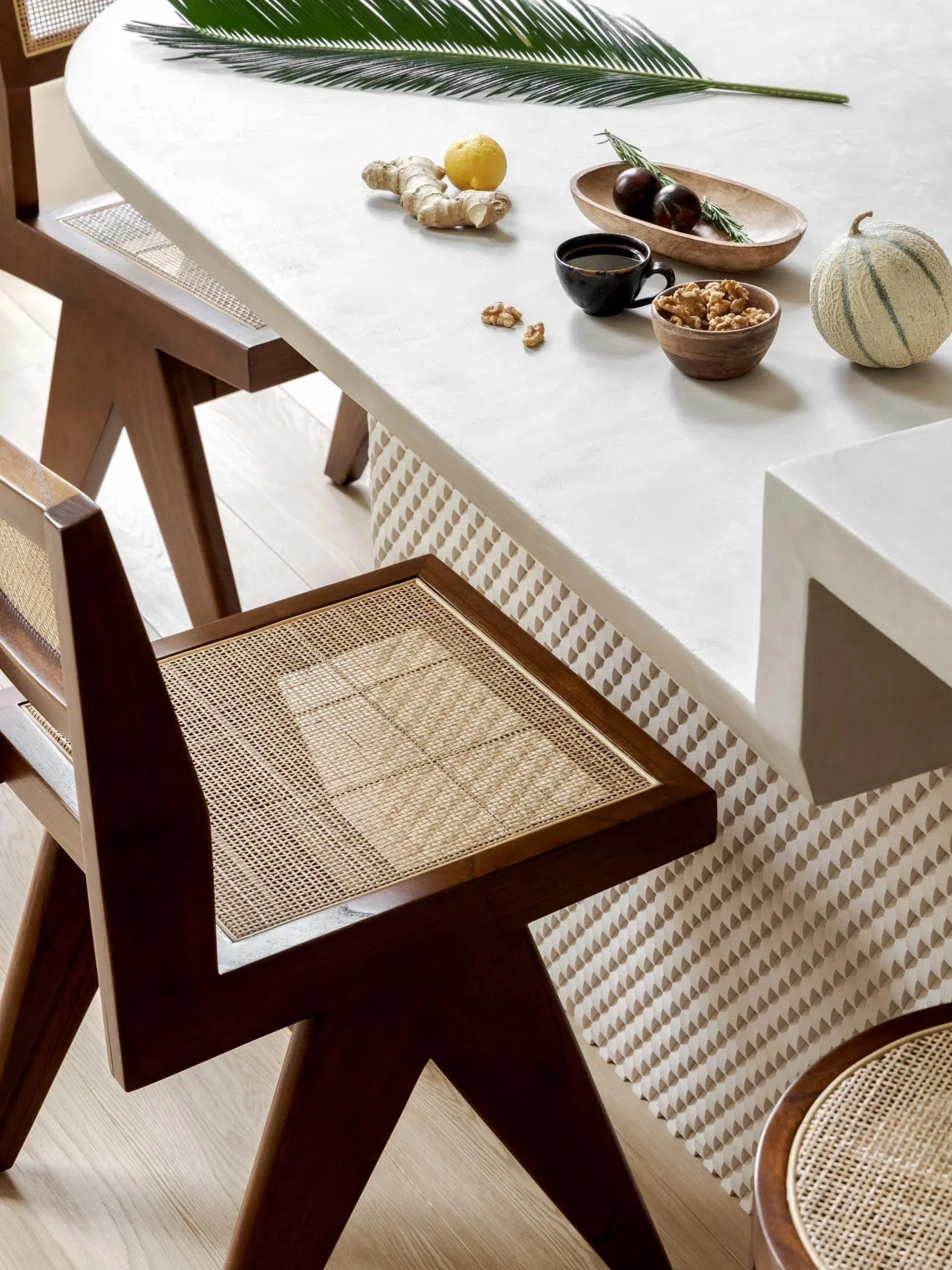 Close-up of a sculptural dining table in London, featuring a textured plaster surface, woven rattan chairs, and natural elements like ginger, walnuts, and fresh herbs for an organic aesthetic.