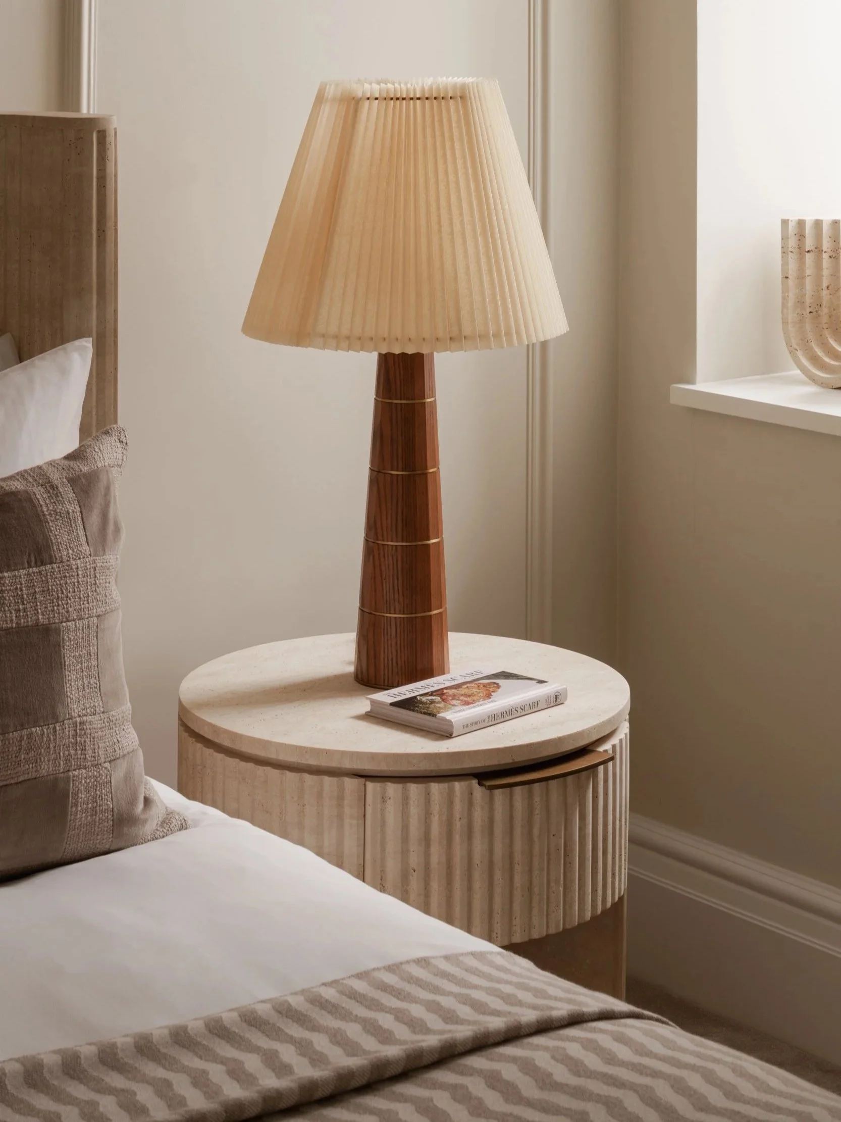 Sophisticated bedroom detail in Knightsbridge, London, featuring a contemporary wooden lamp, fluted stone bedside table, and luxurious neutral styling, captured by an interiors photographer.