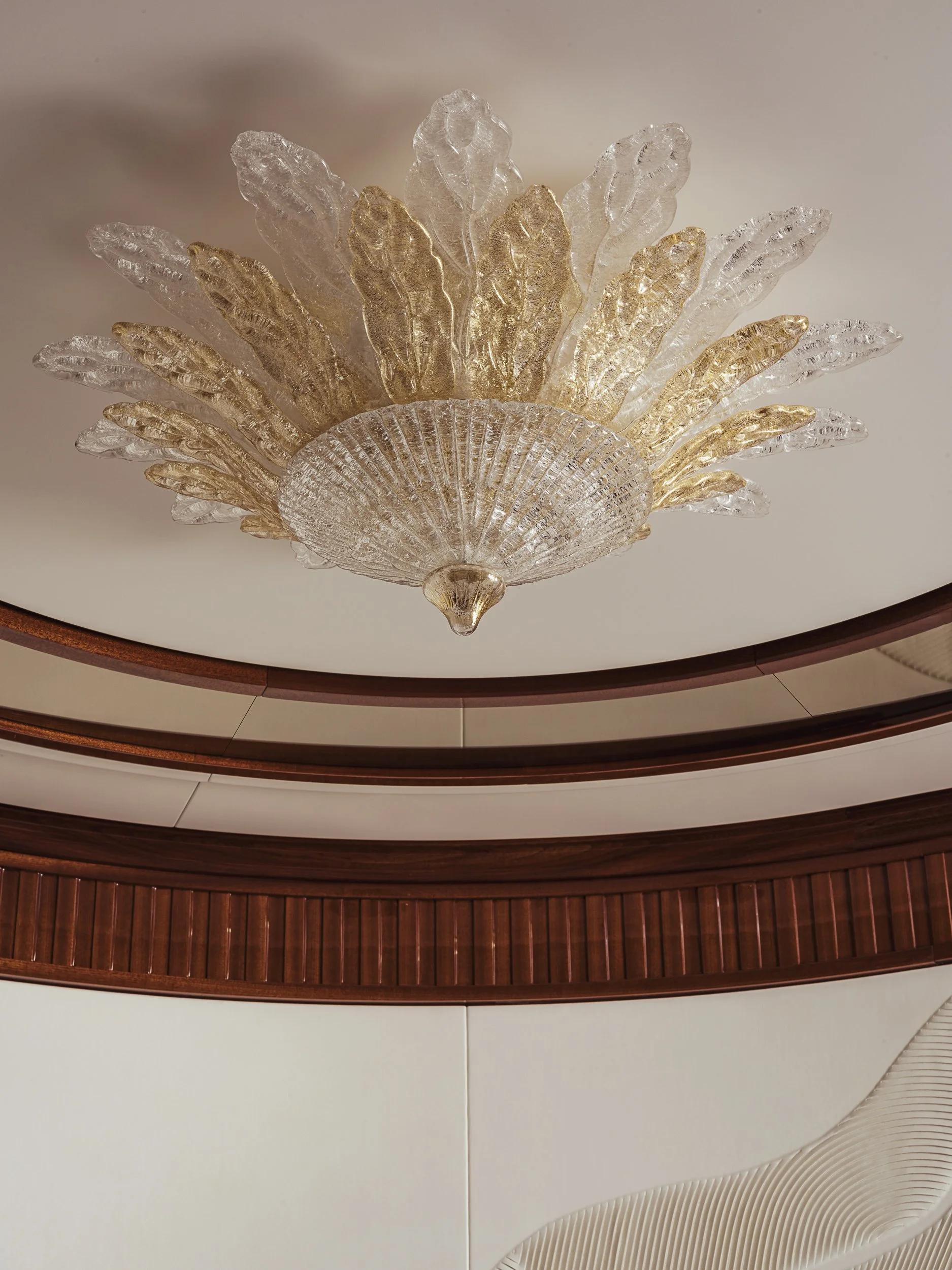 Close-up of a decorative ceiling light fixture with gold and clear glass leaves in a modern interior.