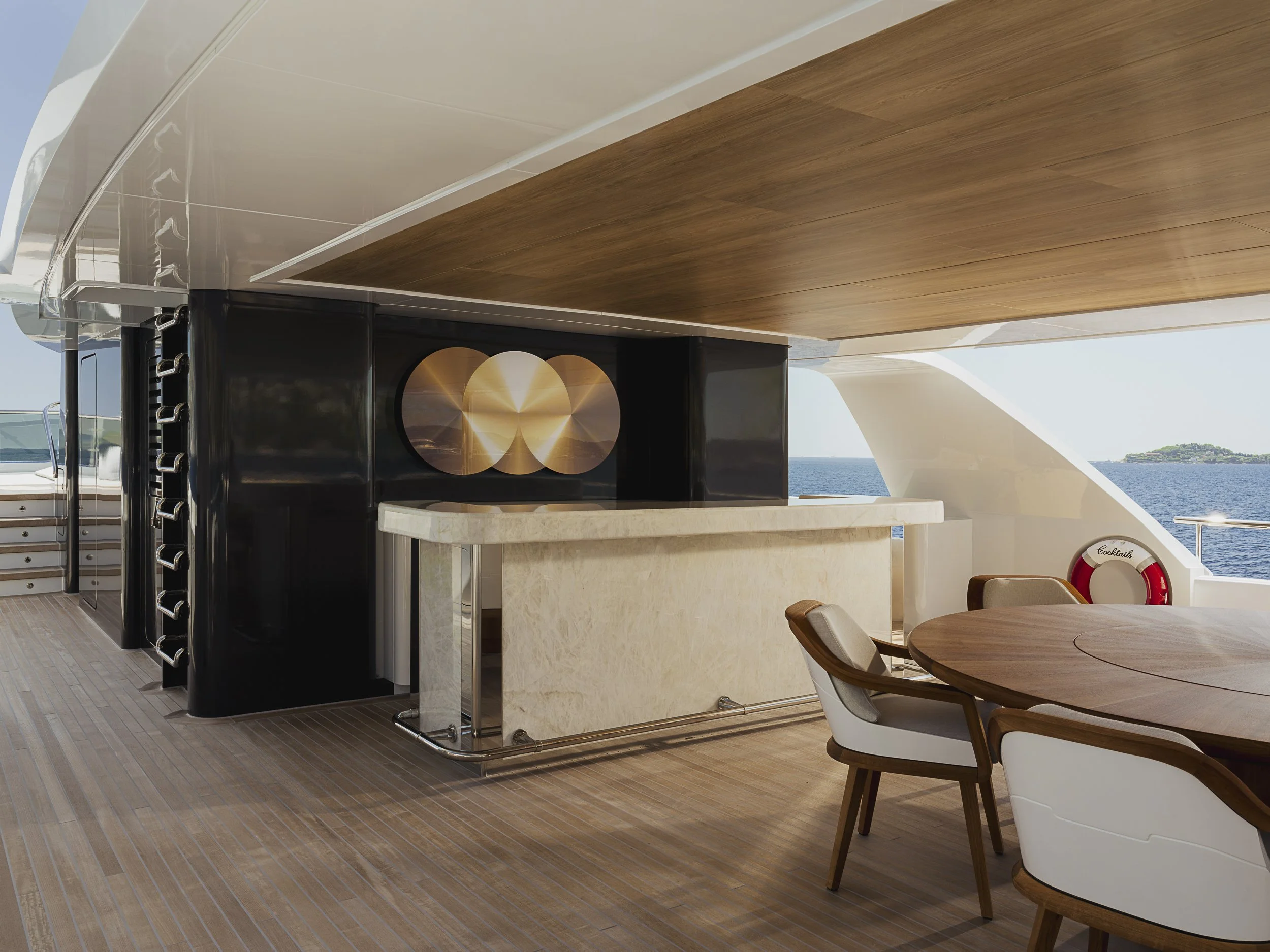 Luxury yacht deck with a wooden ceiling, a black bar with gold circular artwork, a marble counter, and outdoor seating overlooking the ocean.