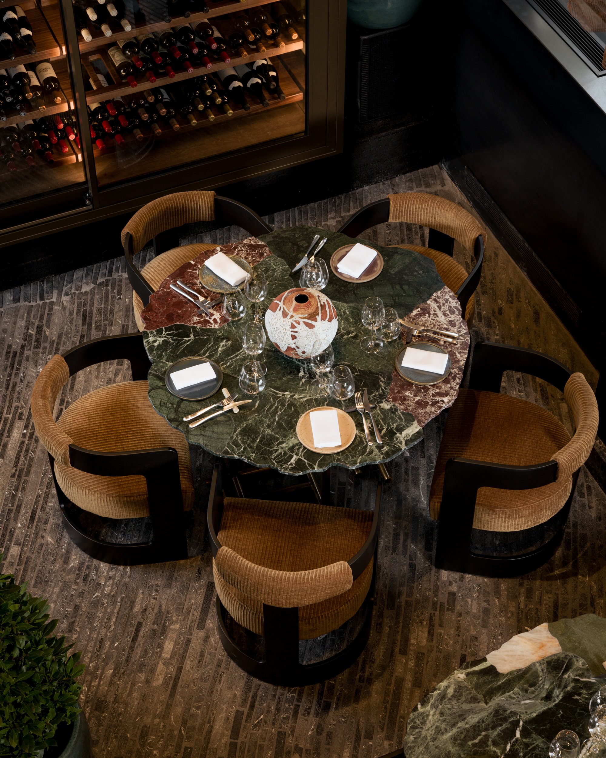 Overhead view of a sculptural marble dining table with mixed stone surfaces, surrounded by upholstered chairs and wine display, photographed by a London interior photographer specialising in hospitality and interior design photography.