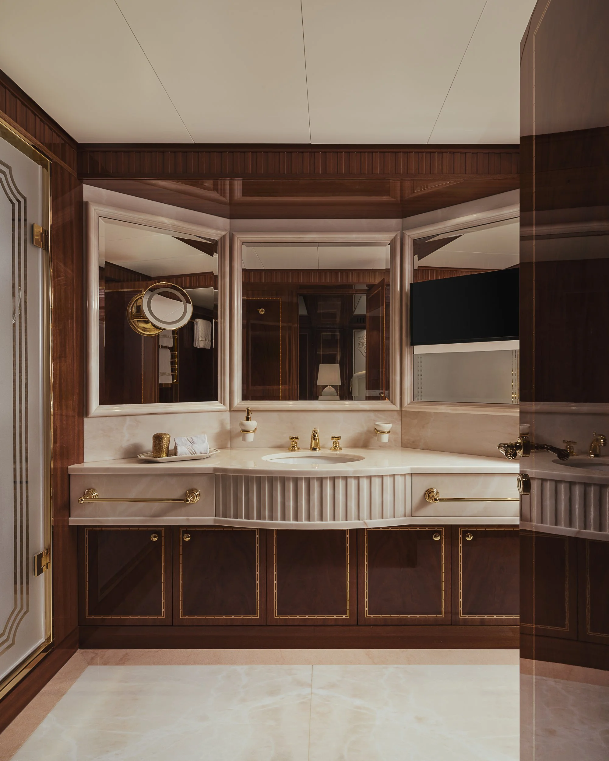 Bathroom with a marble countertop, gold fixtures, three mirrored doors, and wood-paneled walls.