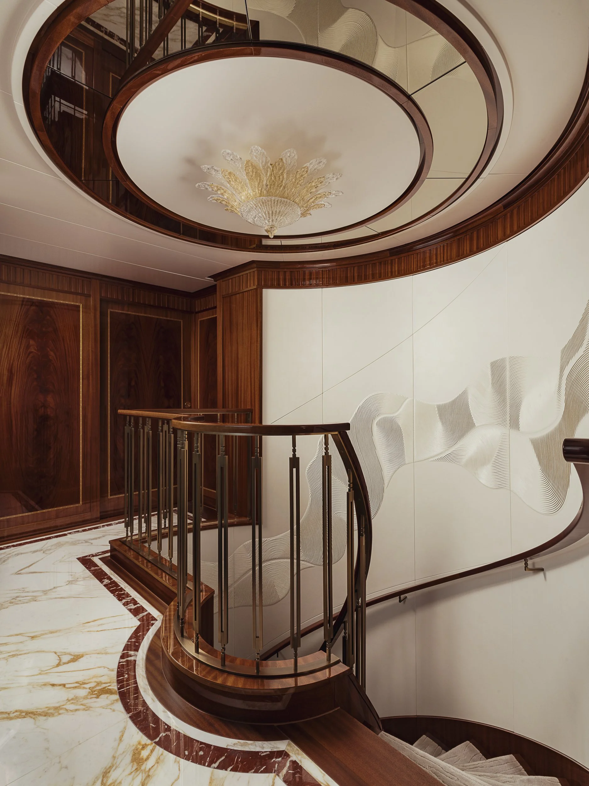 A spiral staircase with wooden handrails and metal balusters, leading downwards, inside a luxurious interior with marble flooring, and an ornate chandelier hanging from the ceiling.