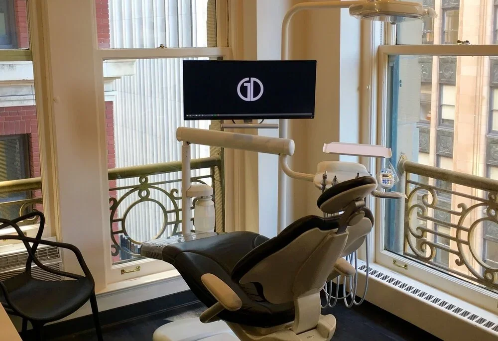 Dental office with a dental chair, monitor, and large windows with decorative iron railings.