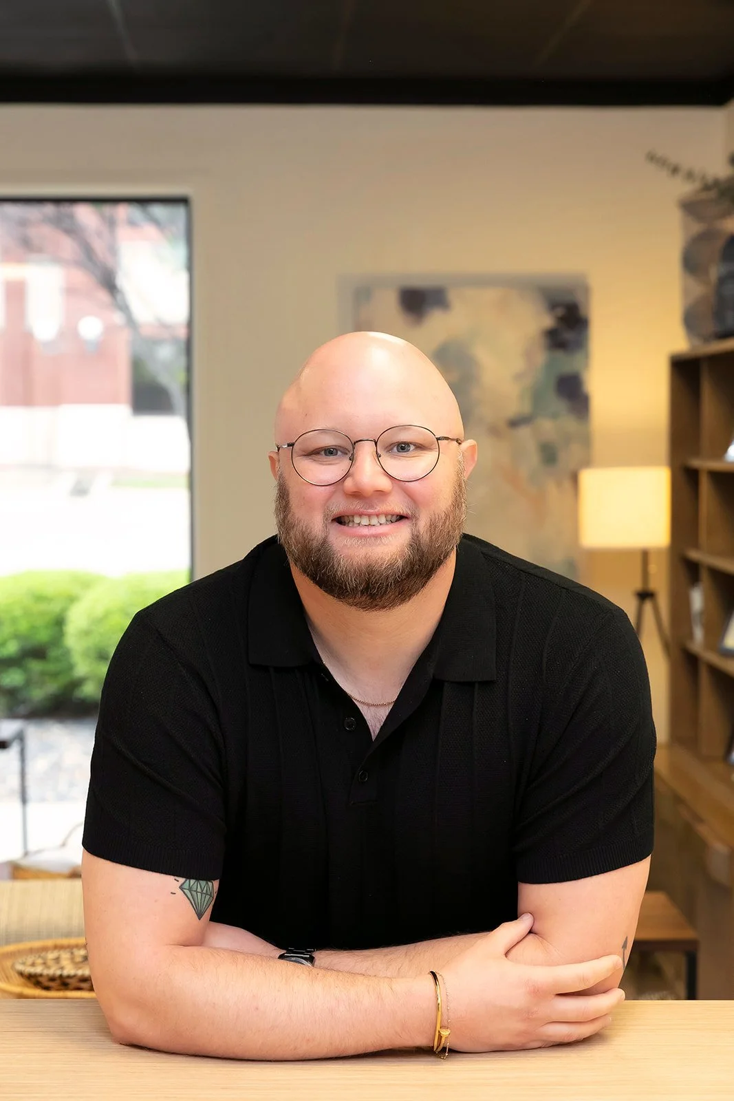 A smiling man with a beard and glasses leaning on a table. Austin's headshot.