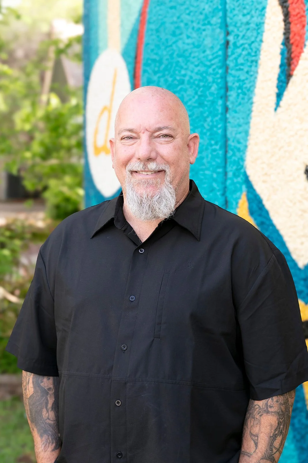 Brian Barton smiling in front of a colorful mural outside