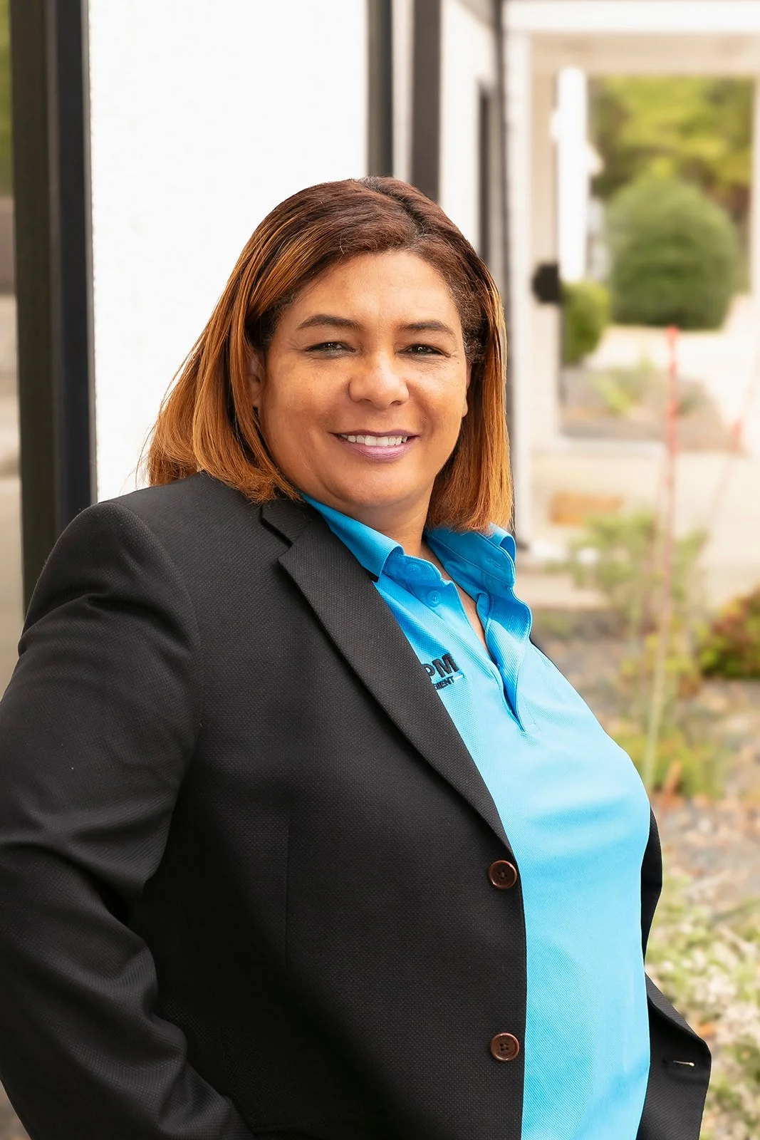 Lisa Freeman leaning on an outside wall smiling in a blue shirt. 
