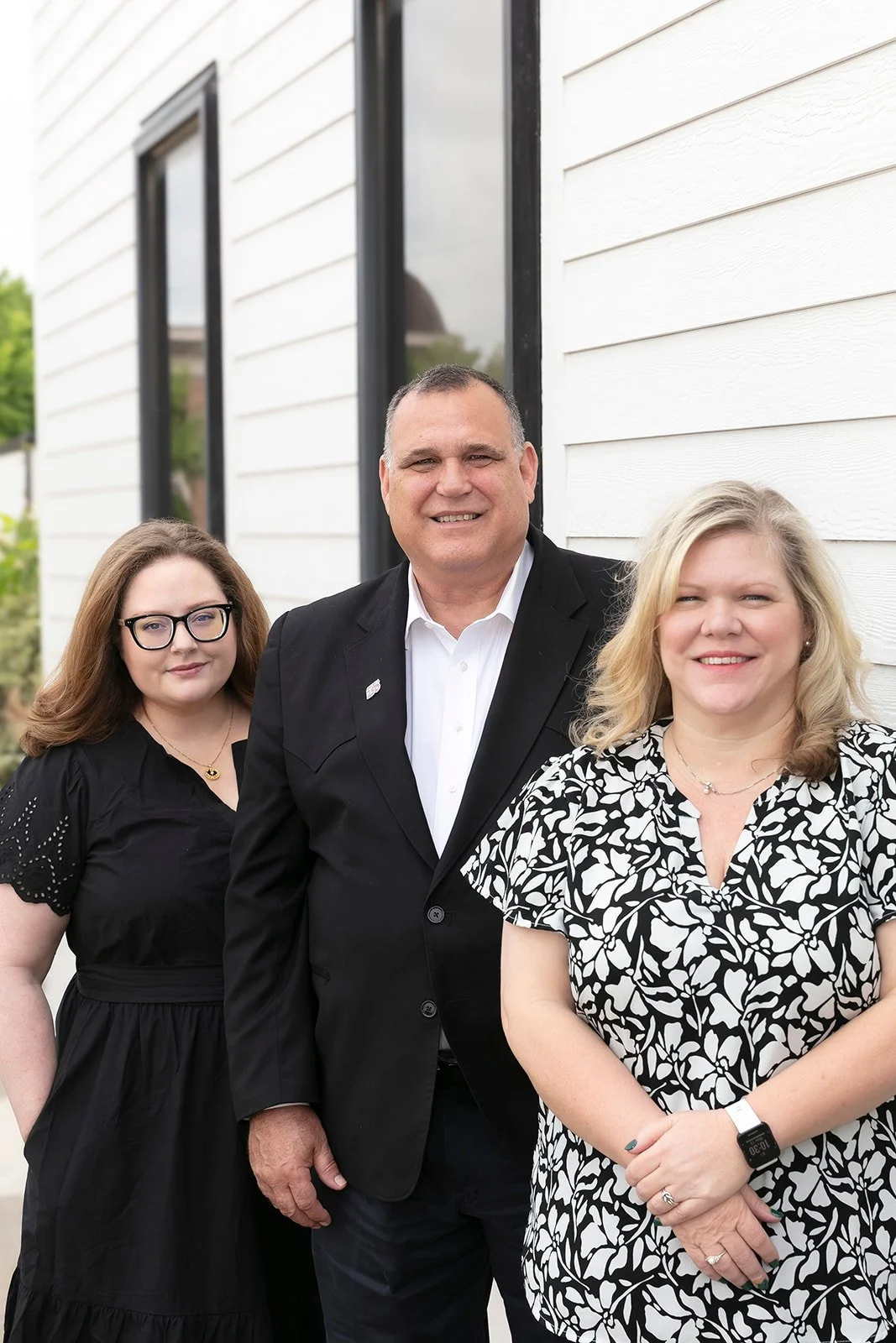 Two women and one man dressed professionally smile outside