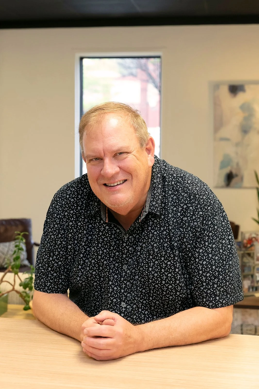 Kyle Voyles headshot in a button up leaning on a table.