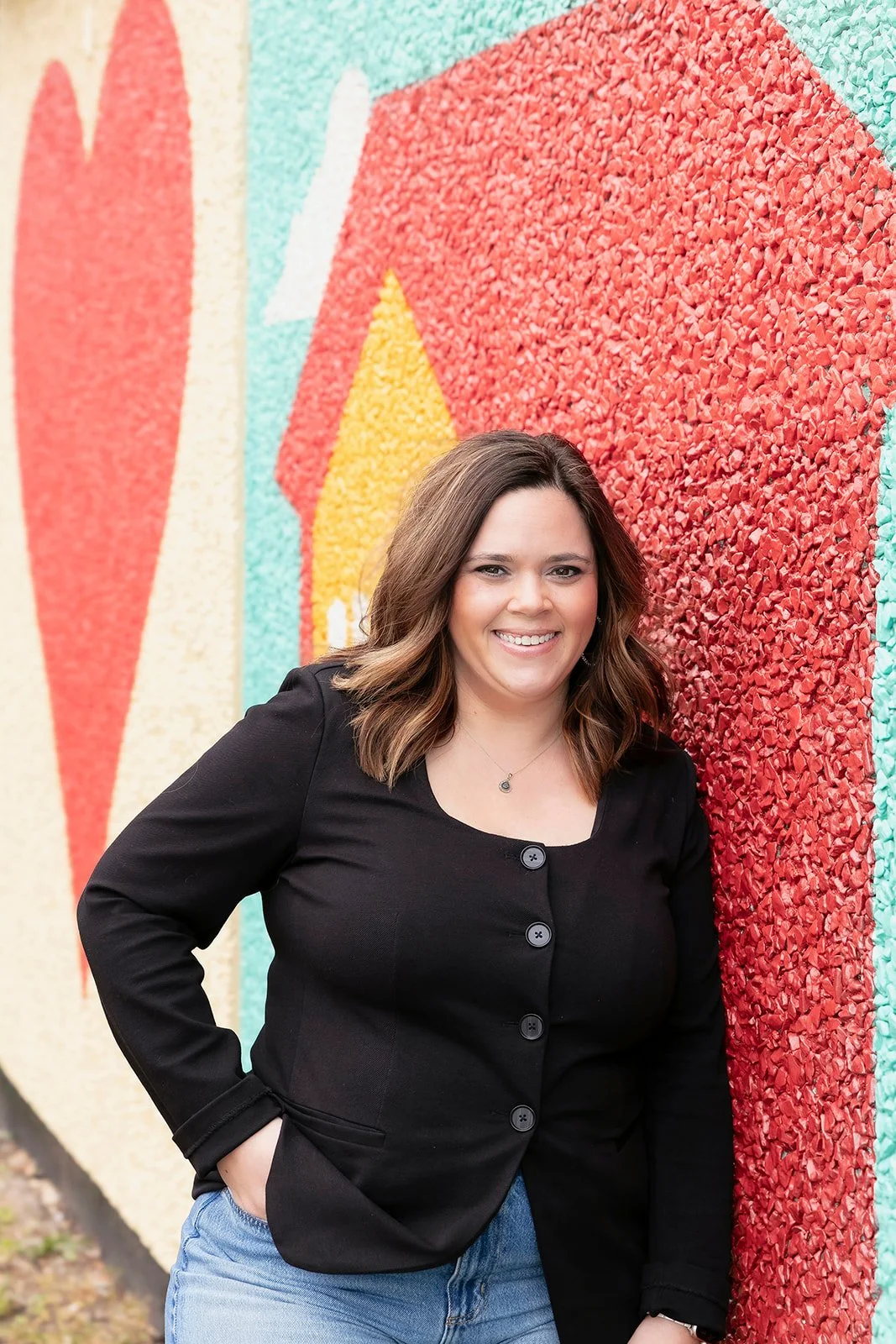 Taylor Brakefield smiling and leaning on a colorful wall mural