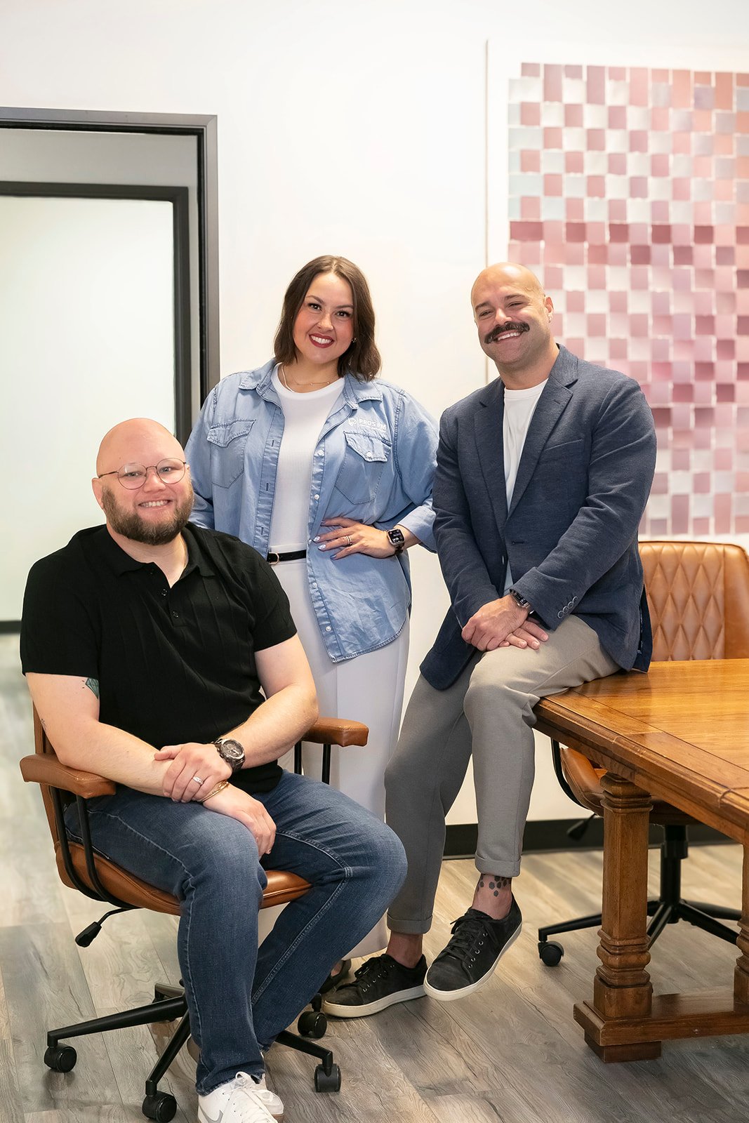 Two men and one woman sitting and standnig around a table smiling
