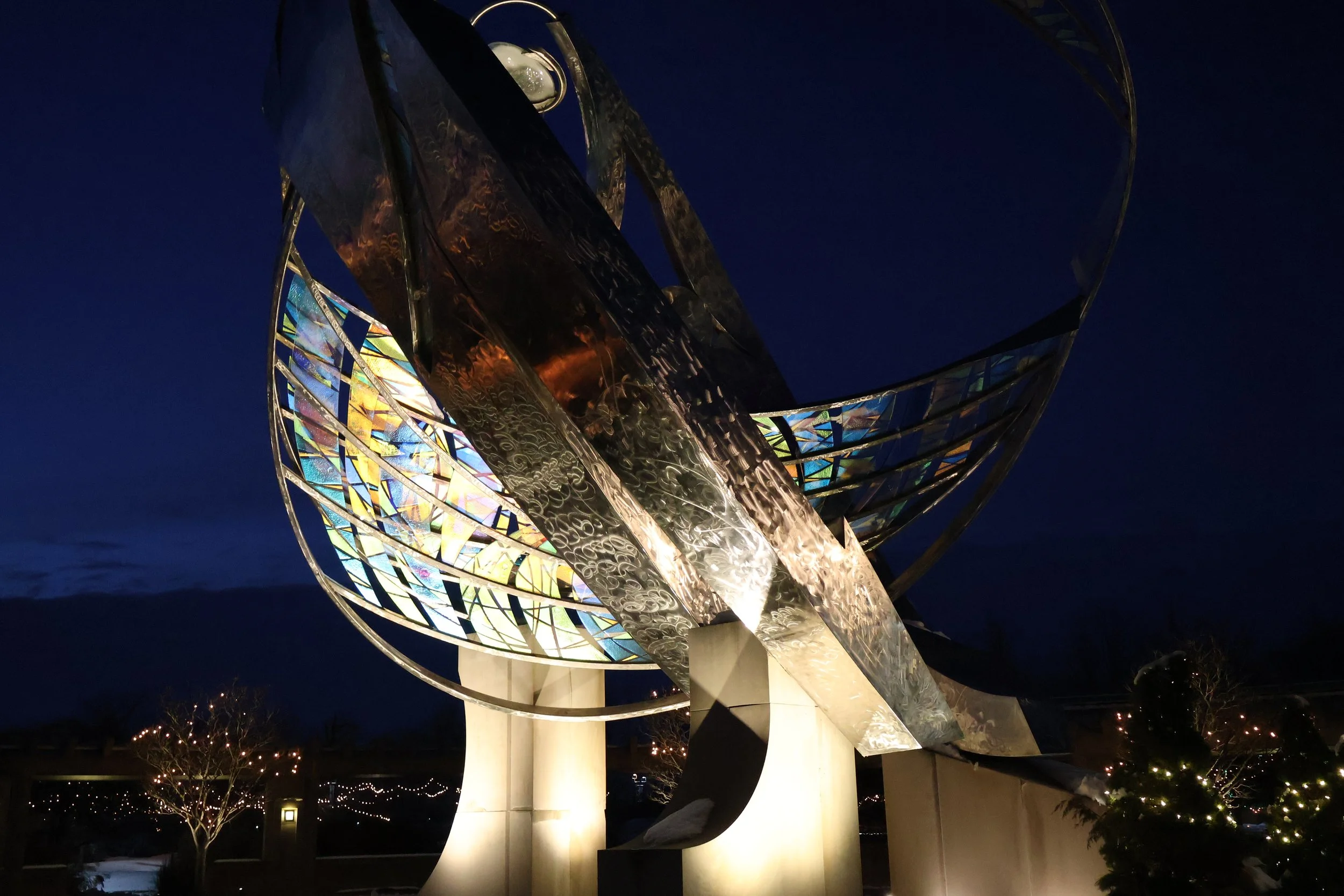 Catalyst sculpture at night with christmas lights behind it.