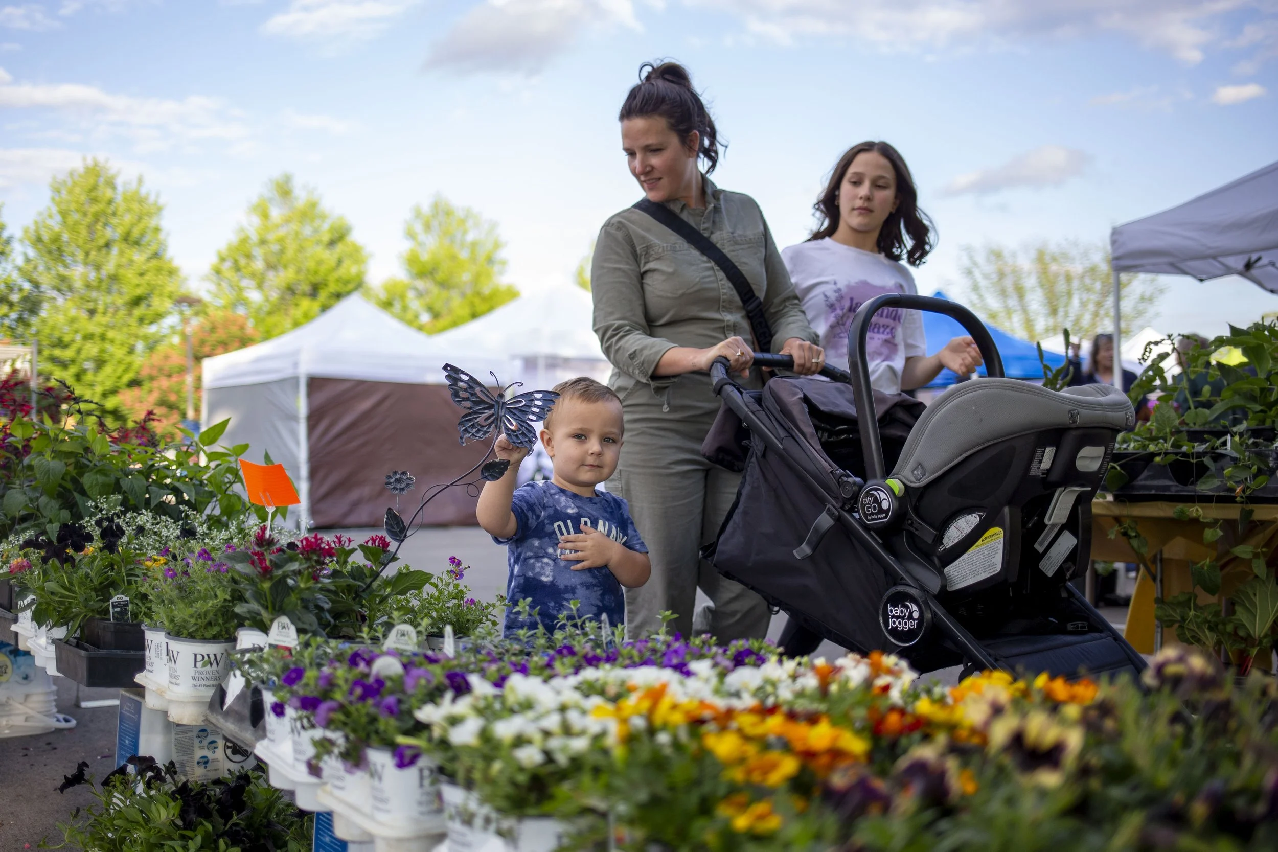 Mother with her kids pushing a stroller in font of flower pots for sale.