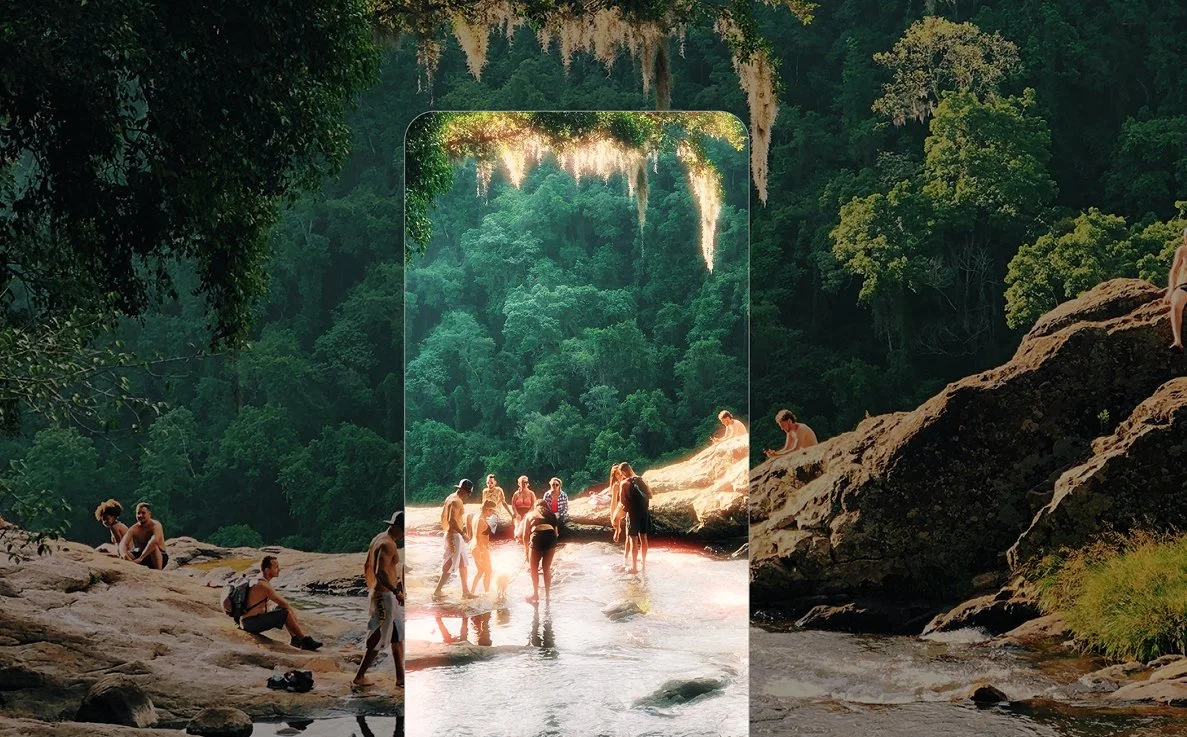 People swimming and relaxing in a river surrounded by dense forest, with a large rock formation and lush greenery in the background.