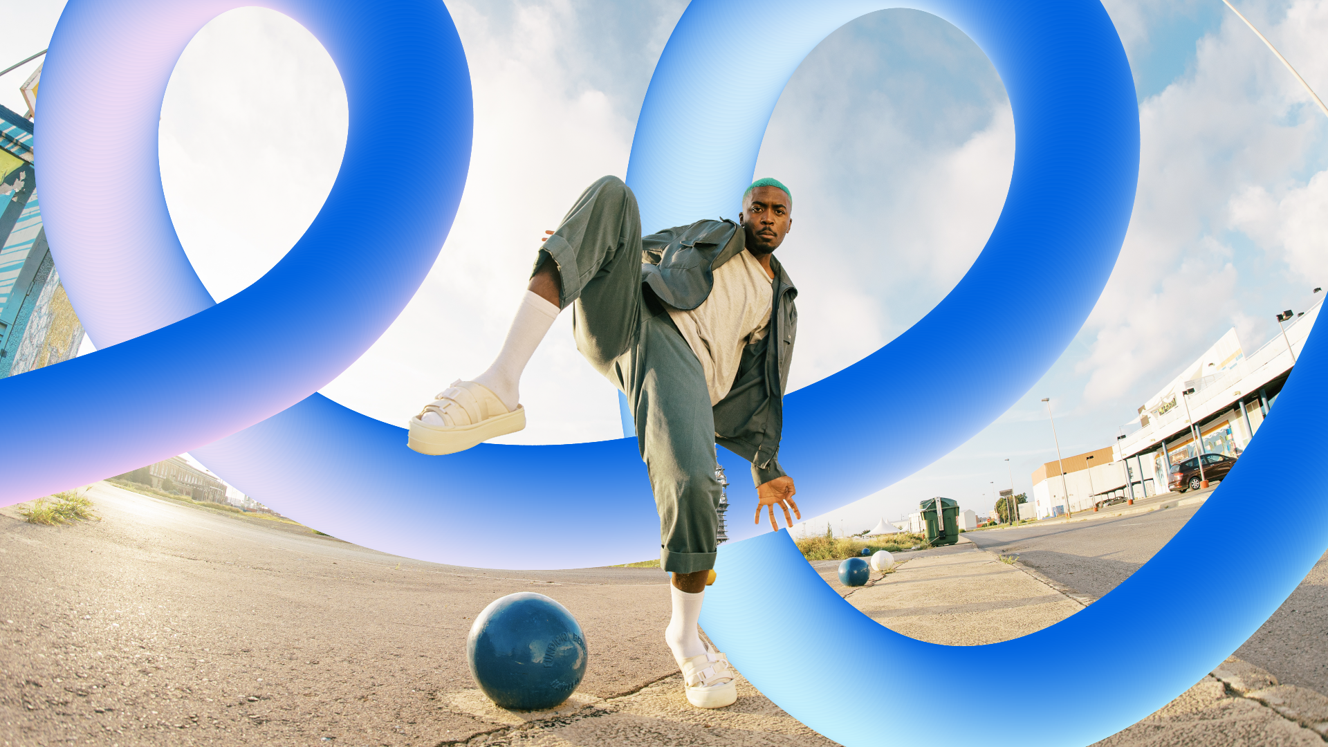 A young man with dyed blue hair wearing a beige t-shirt, green jacket, green pants, and white sandals, crouches on one leg on a sidewalk amid blue abstract loops, with buildings and a parking lot in the background under a partly cloudy sky.