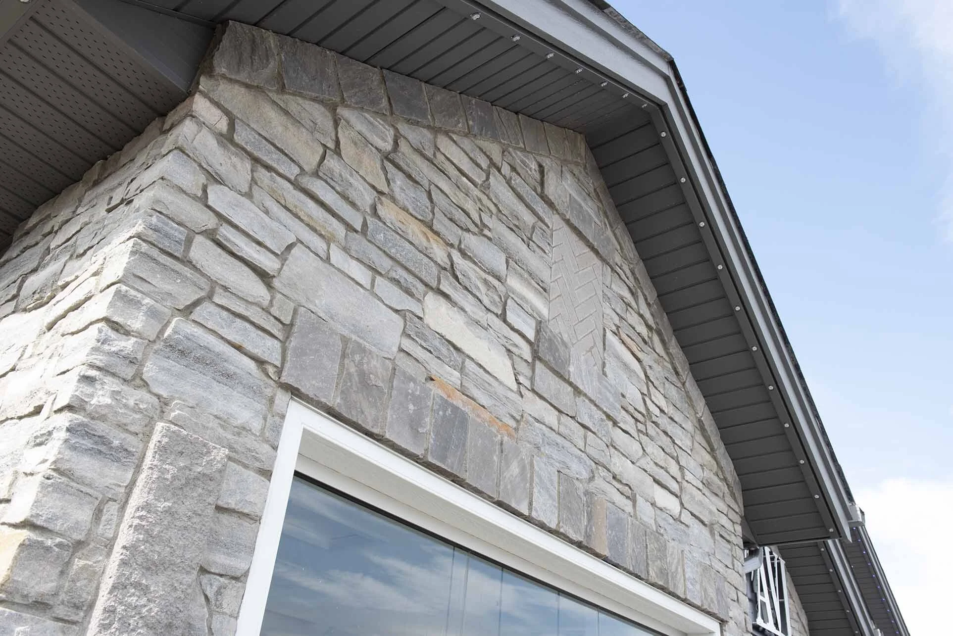 Close-up of a building corner with a stone facade and a metal roof overhang, under a partly cloudy blue sky.