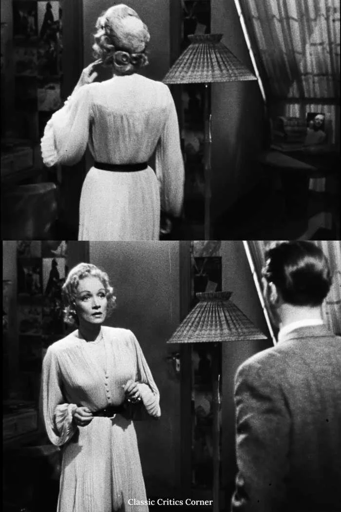 Marlene Dietrich’s character Charlotte Inwood is wearing a beautiful pleated white dress with long billowing sleeves that is cinched at the waist with a black belt. She also has an elegant black overcoat and fur cap. Her jewelry includes diamond ear…