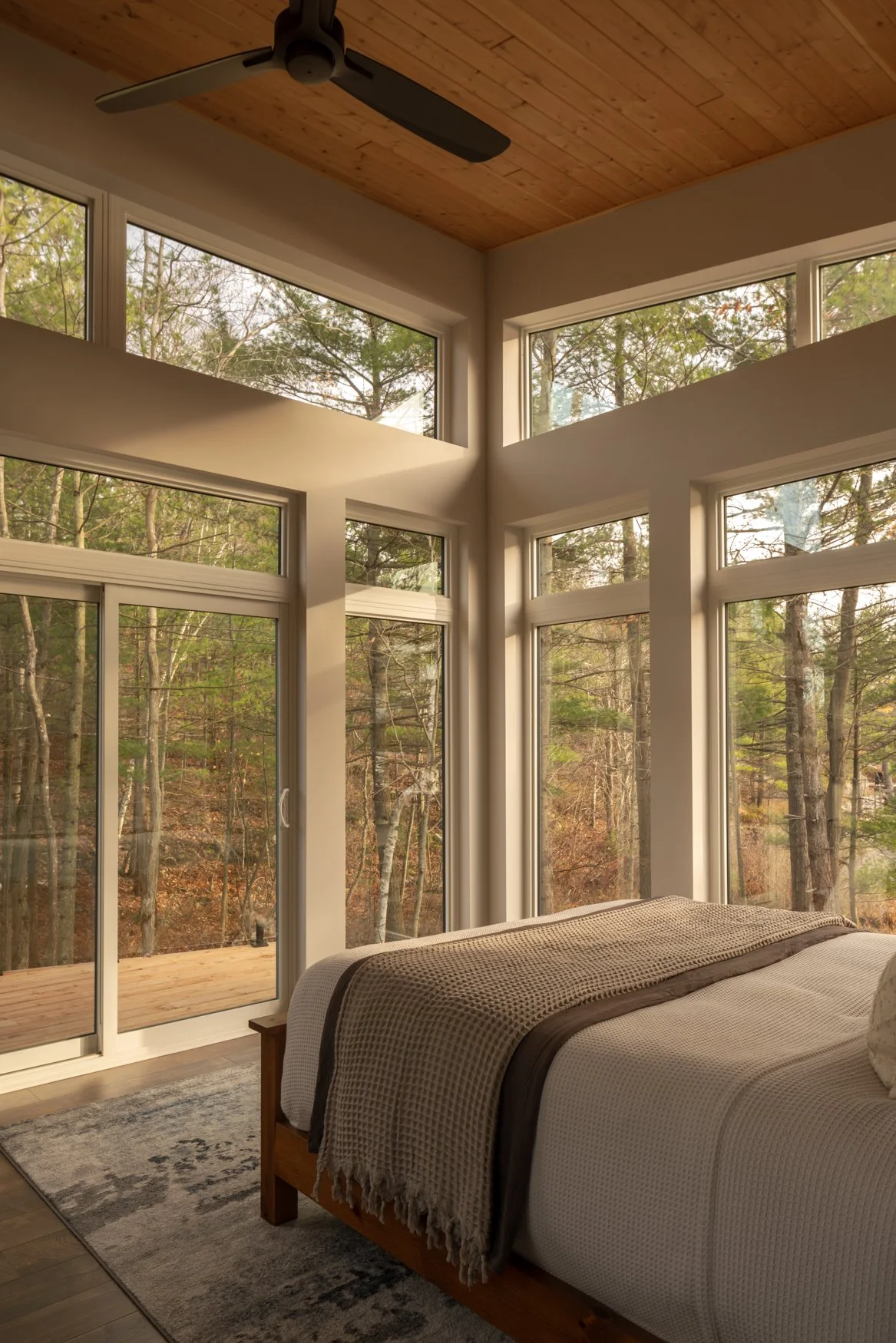 Primary bedroom with floor to ceiling windows capturing picturesque forest and lake views