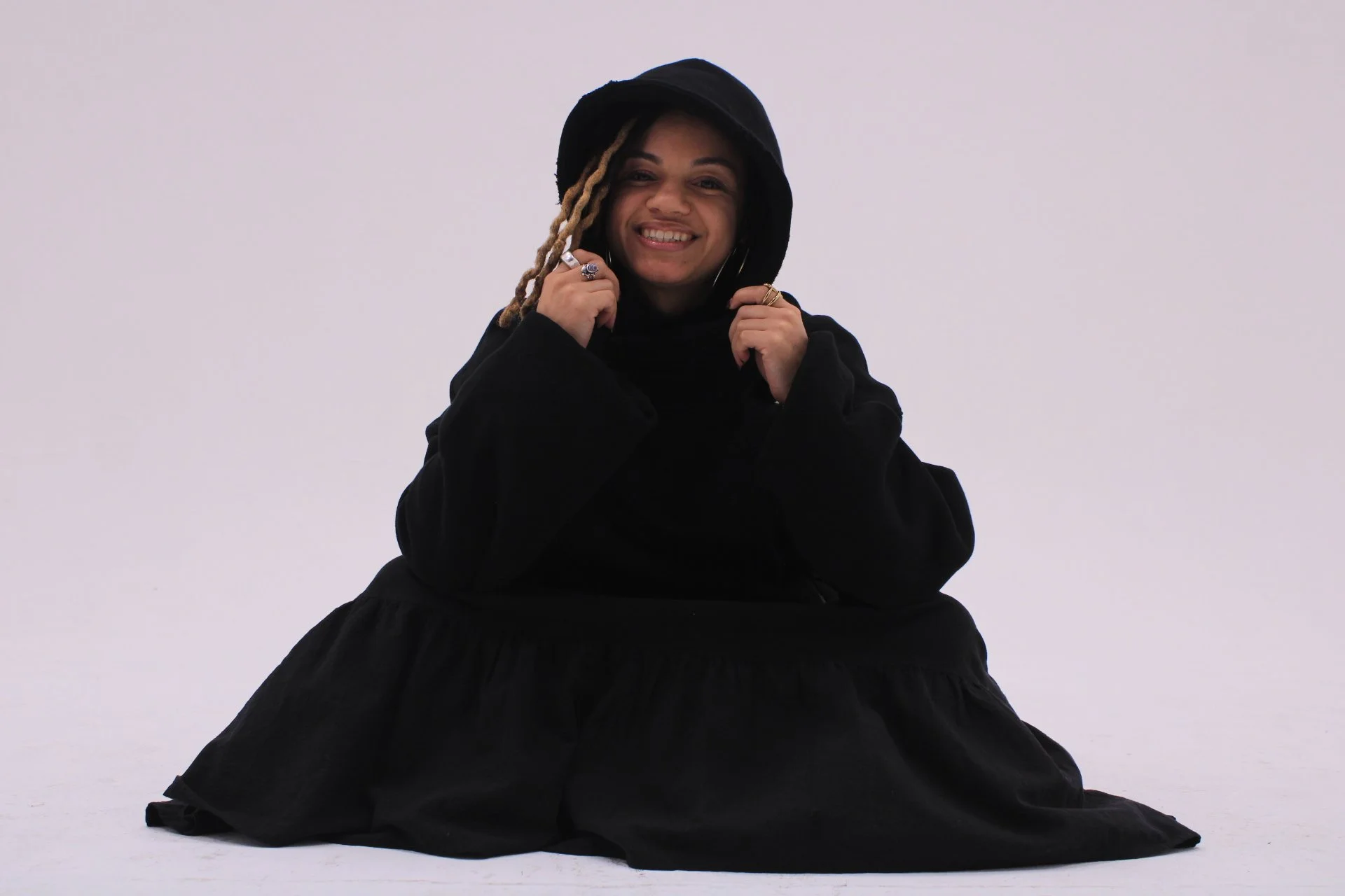 Woman smiling in an oversized black VOUFO hoodie, seated against a lilac backdrop