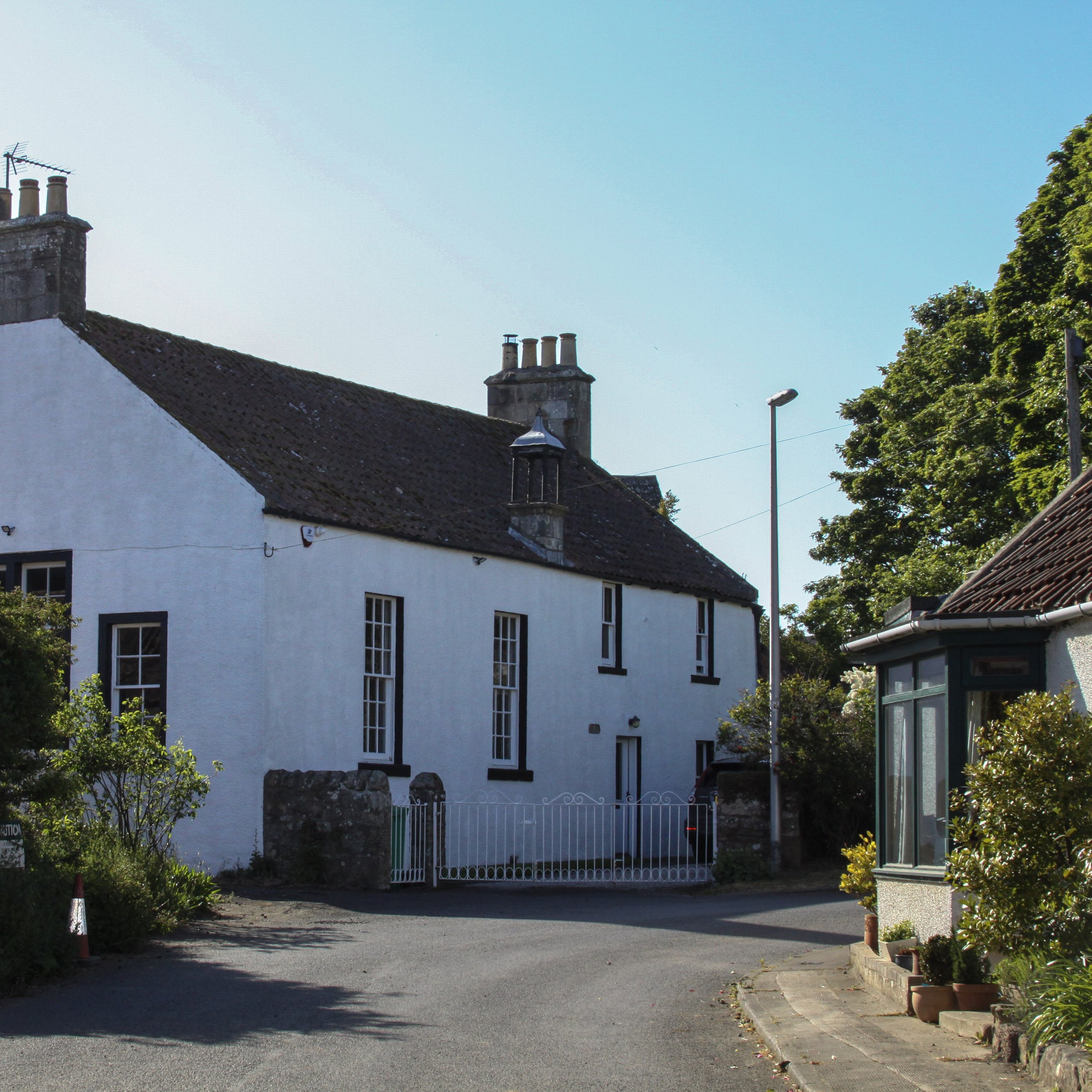 A traditional white house with a pitched roof, multiple chimneys, and tall narrow windows, surrounded by greenery on a sunny day.