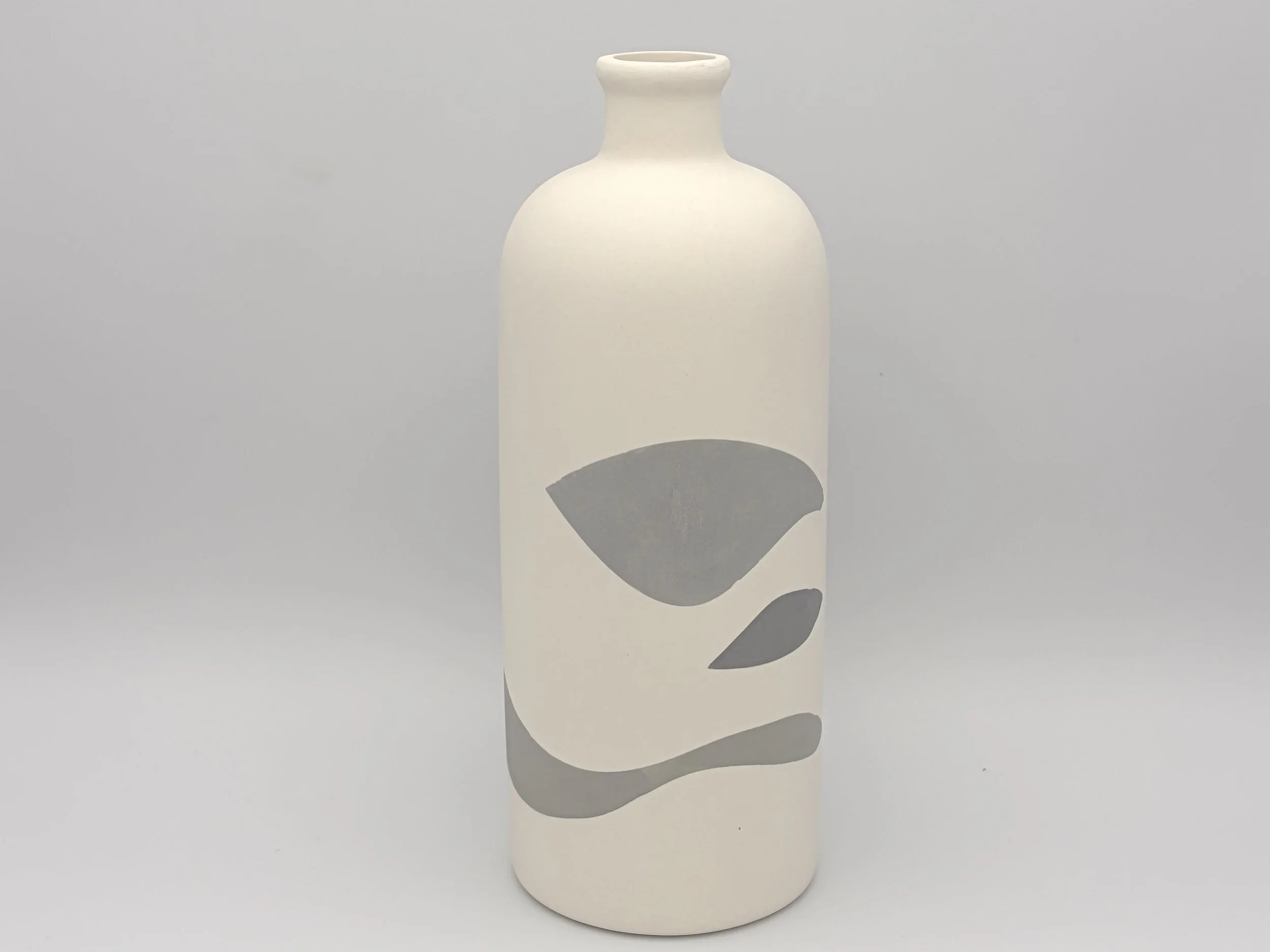 A minimalist, abstract ceramic vase with a narrow neck, rounded body, and a smooth matte white finish, casting shadows on a light grey background.