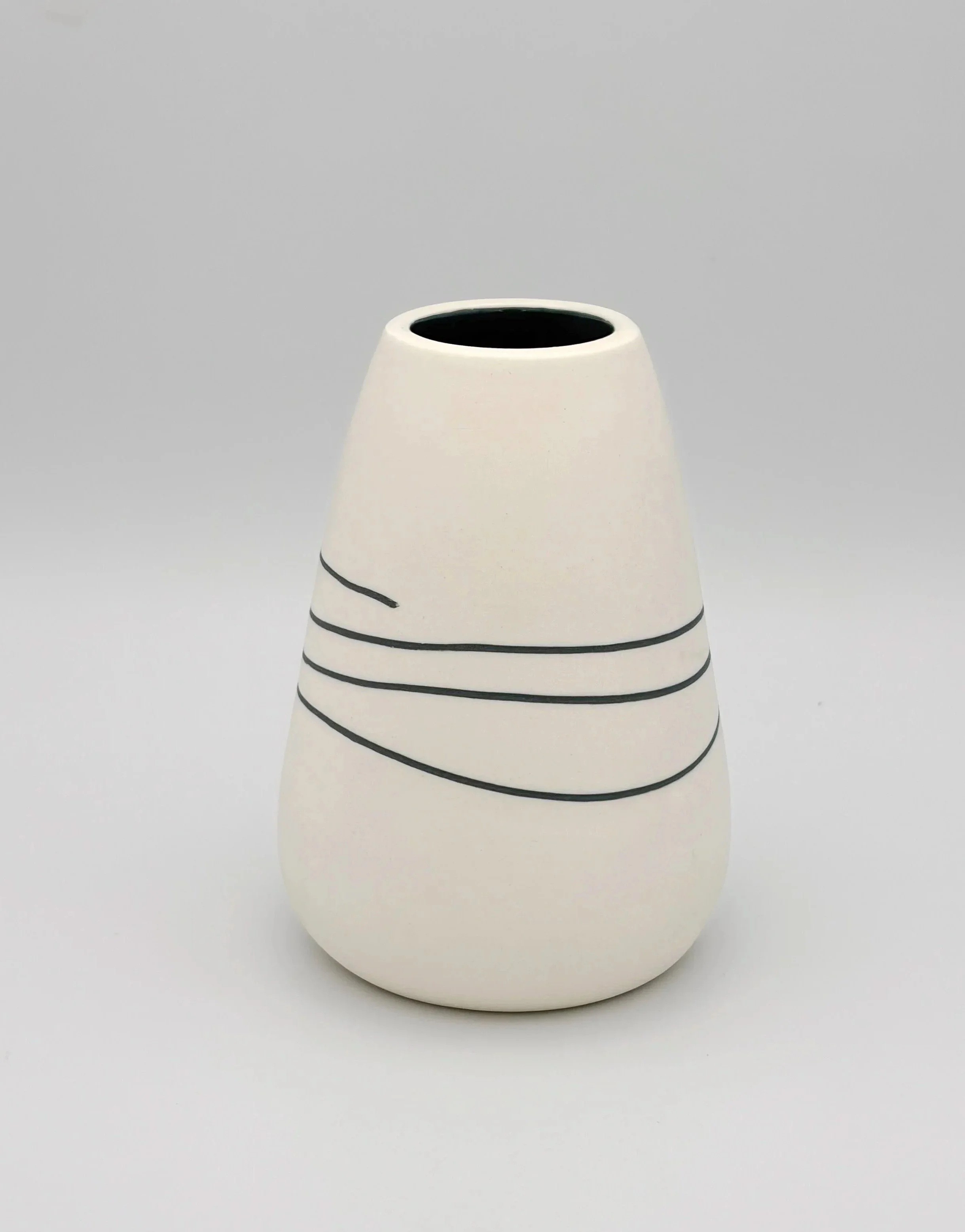 A white ceramic vase with black spiral line decorations, blurred, with a blank gray background.