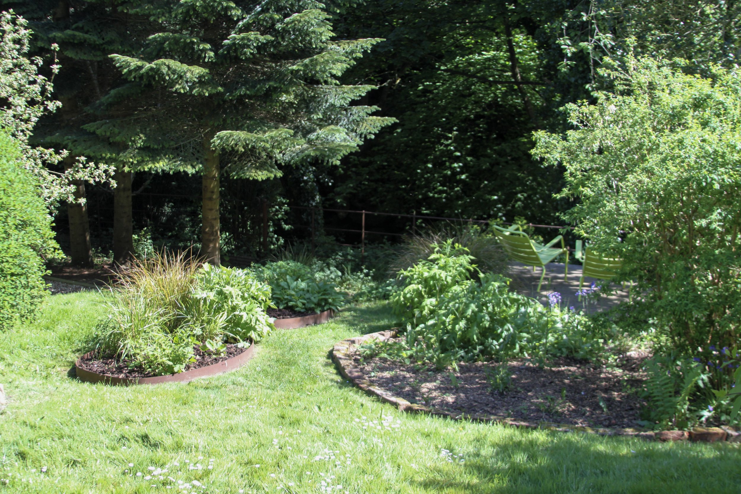 A lush garden with green plants, trees, and a small sitting area with chairs in the background.